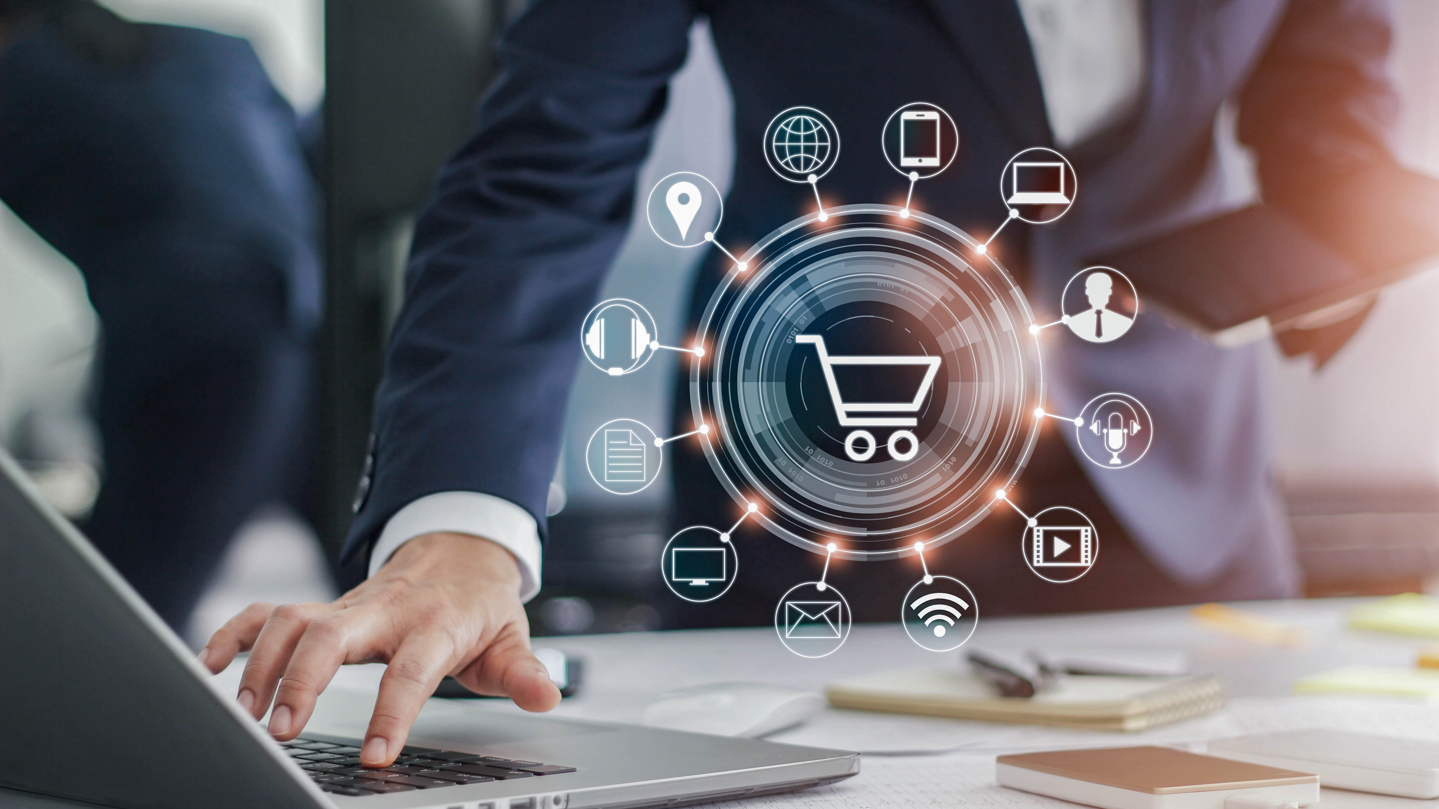 Hände eines Mannes in Anzug, die auf einem Laptop tippen, umgeben von Symbolen für digitale Kommunikation und E-Commerce.