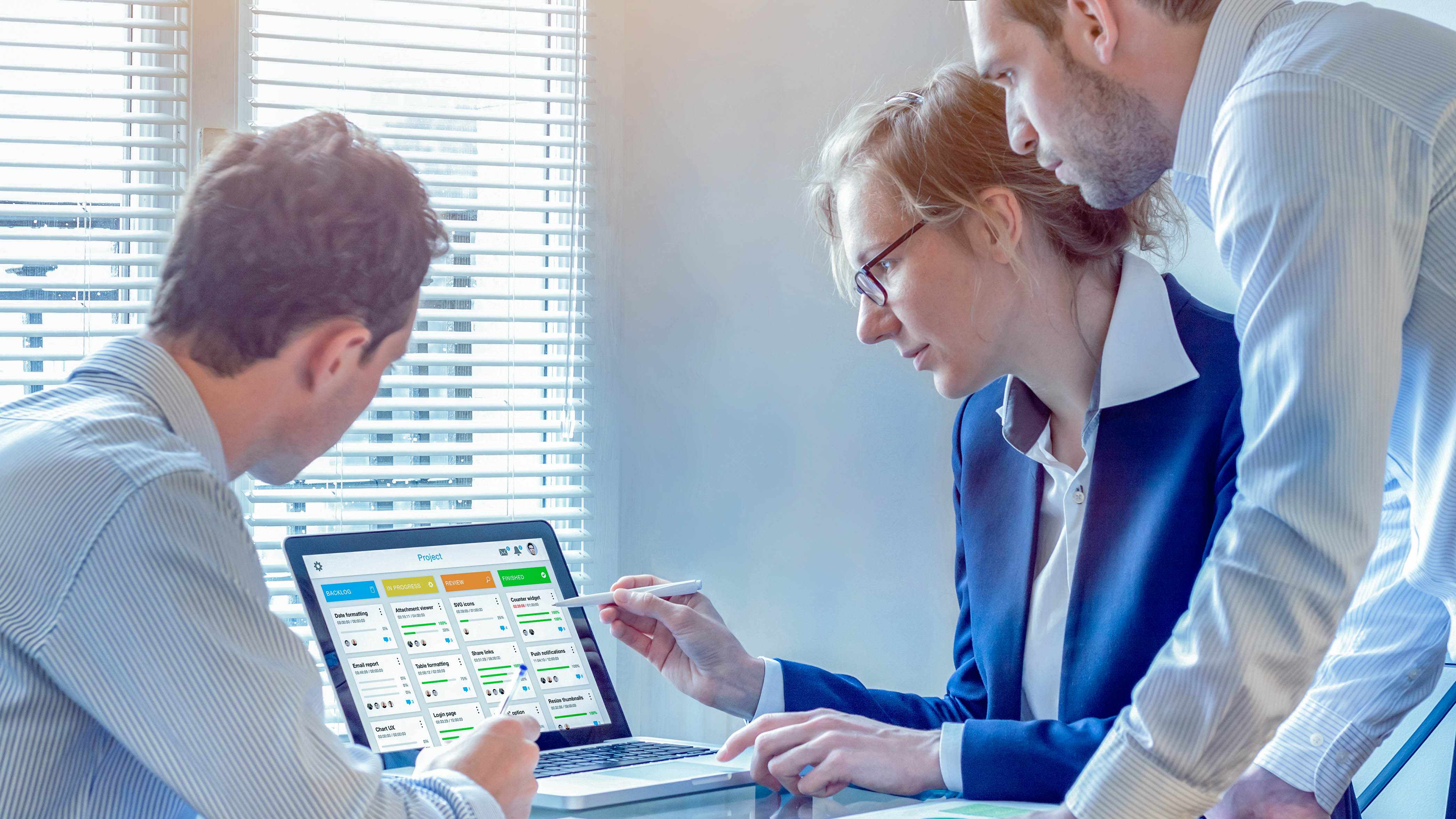 Drei Personen betrachten gemeinsam einen Laptop-Bildschirm mit Projektmanagement-Software.
