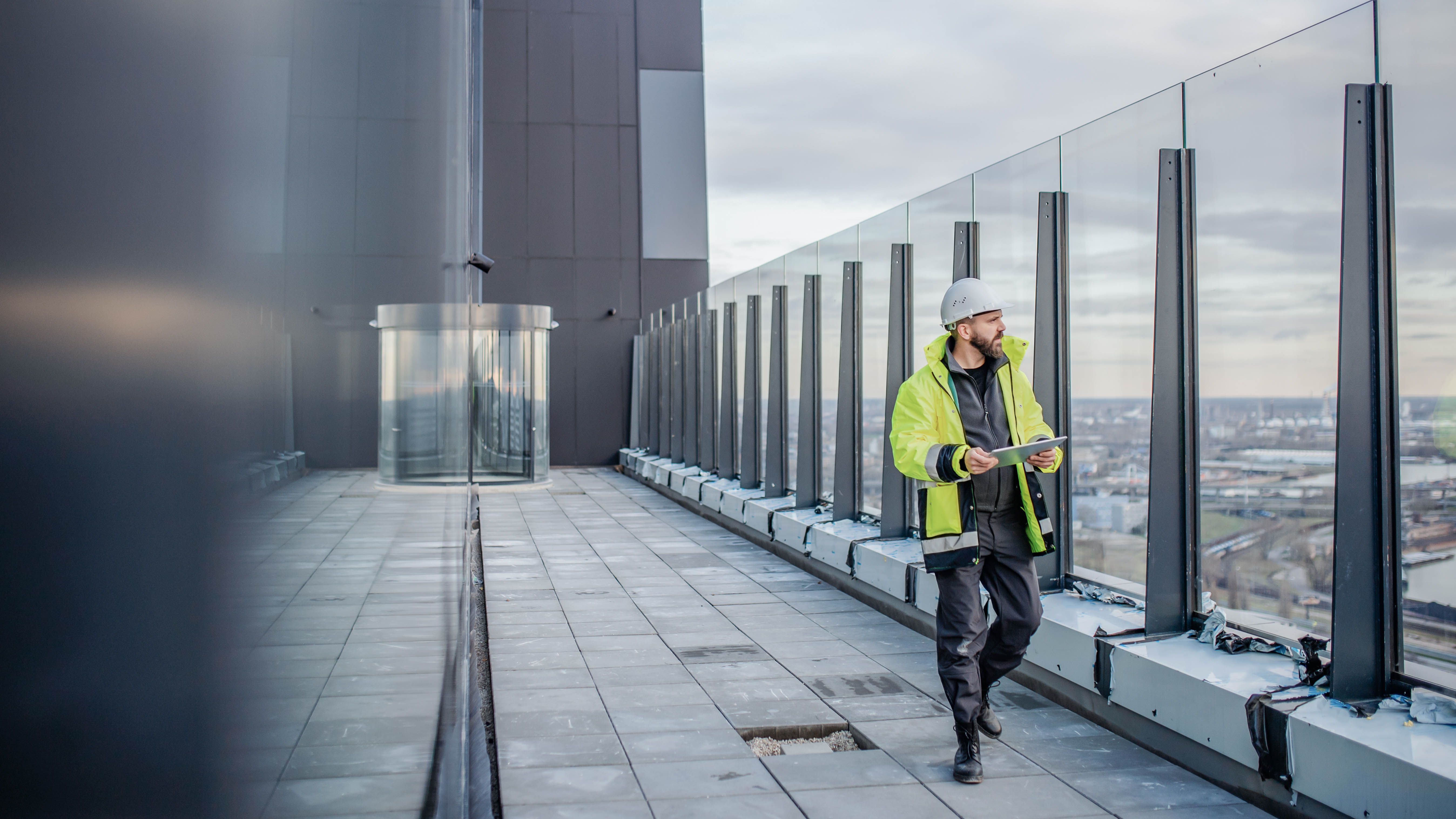 Ein Bauarbeiter in Sicherheitskleidung und Helm steht auf einer Dachterrasse und betrachtet Pläne.