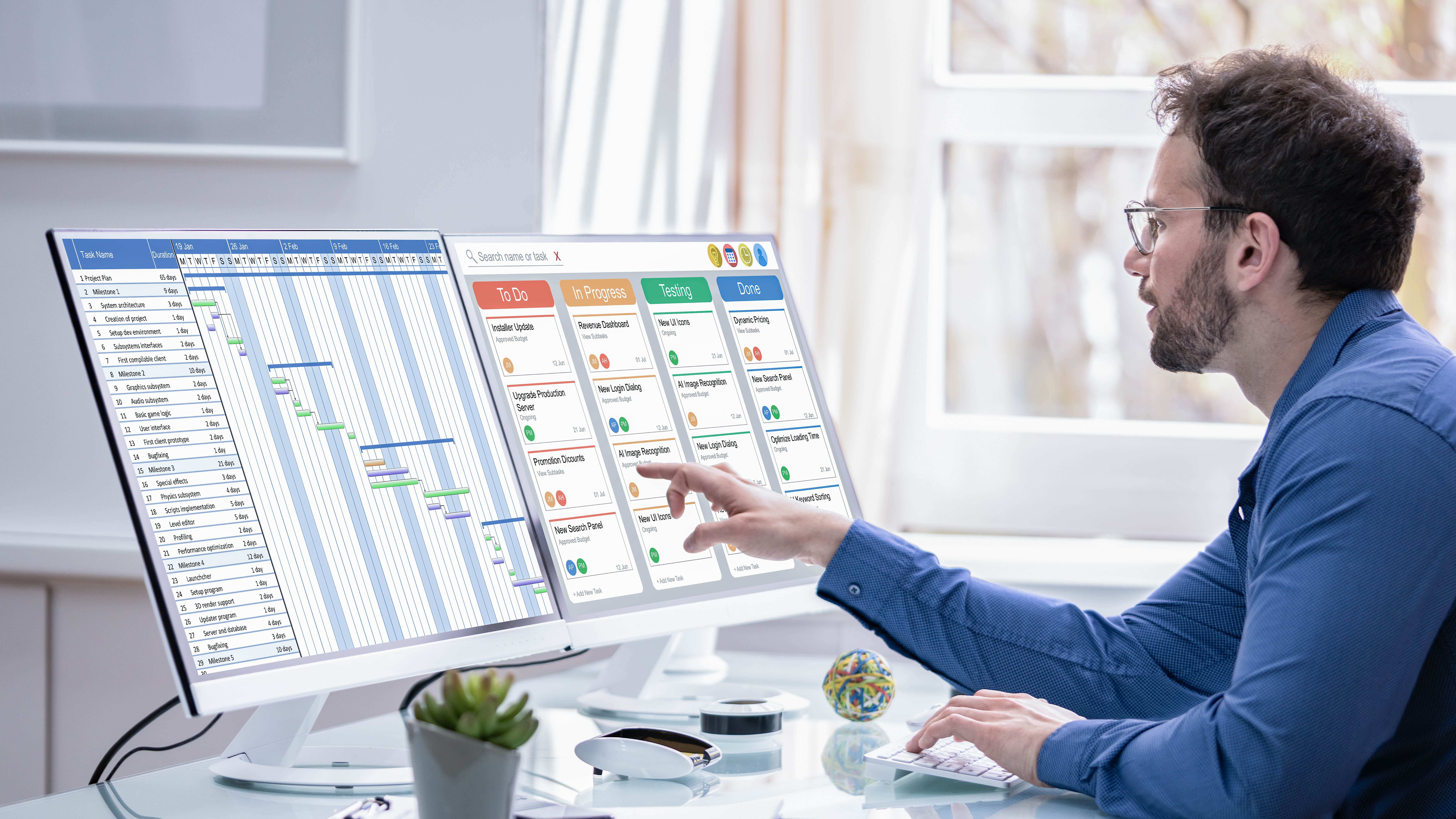 Mann in blauer Hemd sitzt an einem Schreibtisch und arbeitet an zwei Monitoren mit Projektmanagement-Software.
