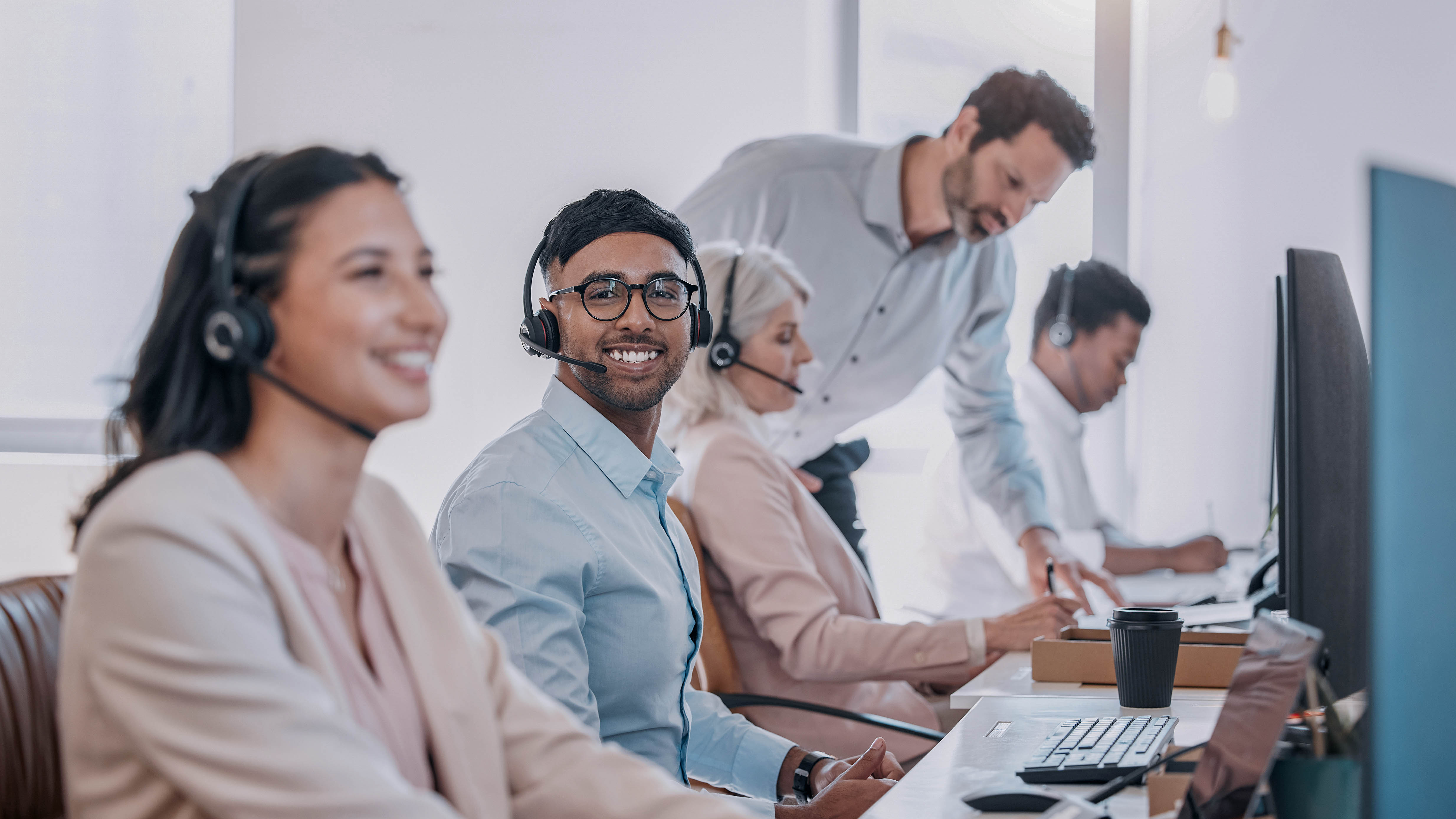 Mitarbeiter in einem modernen Büro mit Headsets, die an Schreibtischen arbeiten und miteinander kommunizieren.