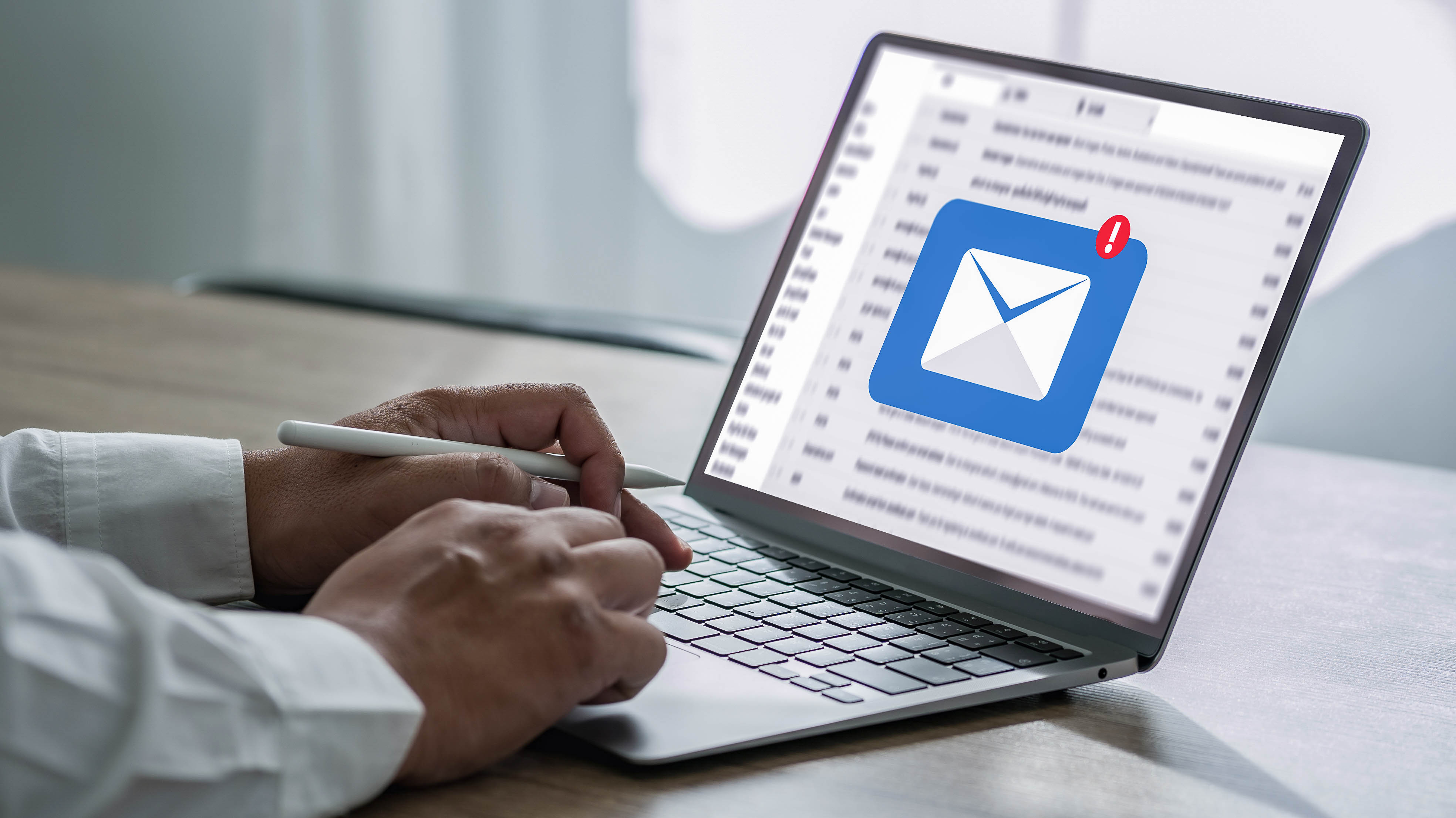 Hände tippen auf einer Laptop-Tastatur, während ein E-Mail-Symbol mit einer Benachrichtigung auf dem Bildschirm angezeigt wird.