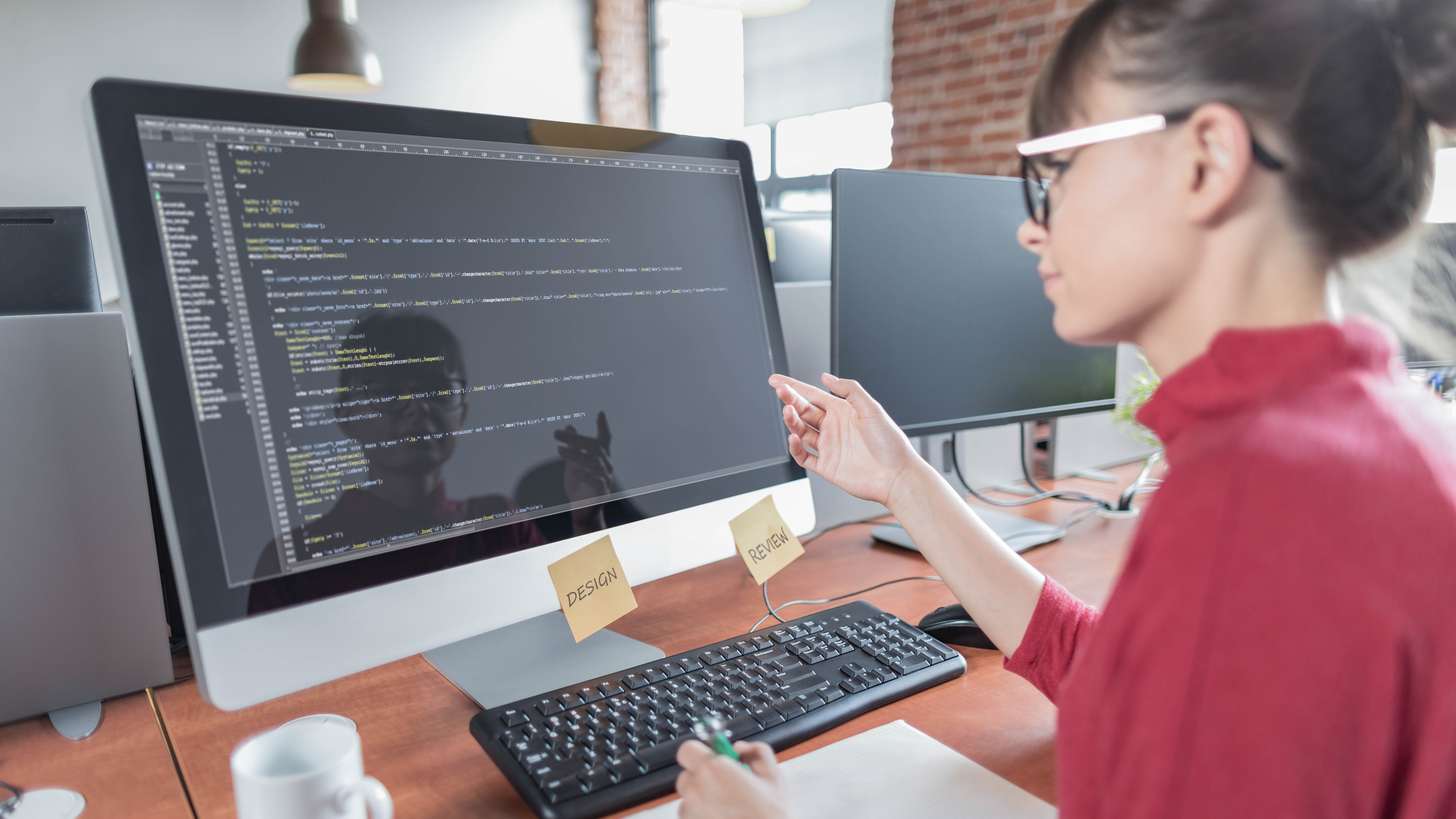 Eine Person sitzt an einem Schreibtisch und zeigt auf einen Computerbildschirm mit Code.