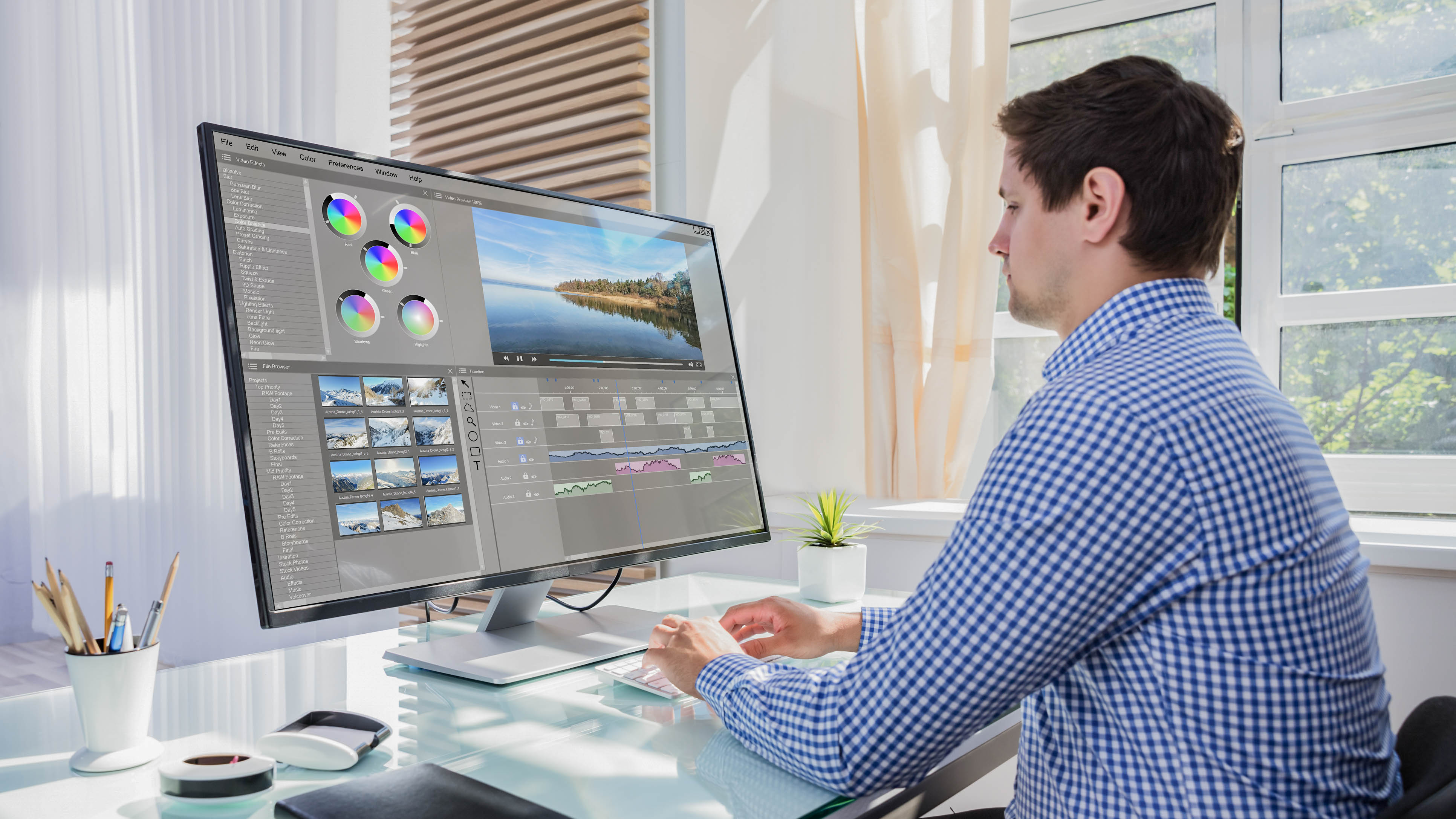 Ein Mann sitzt an einem Schreibtisch und bearbeitet Bilder auf einem großen Monitor mit verschiedenen Werkzeugen und Farbreglern.