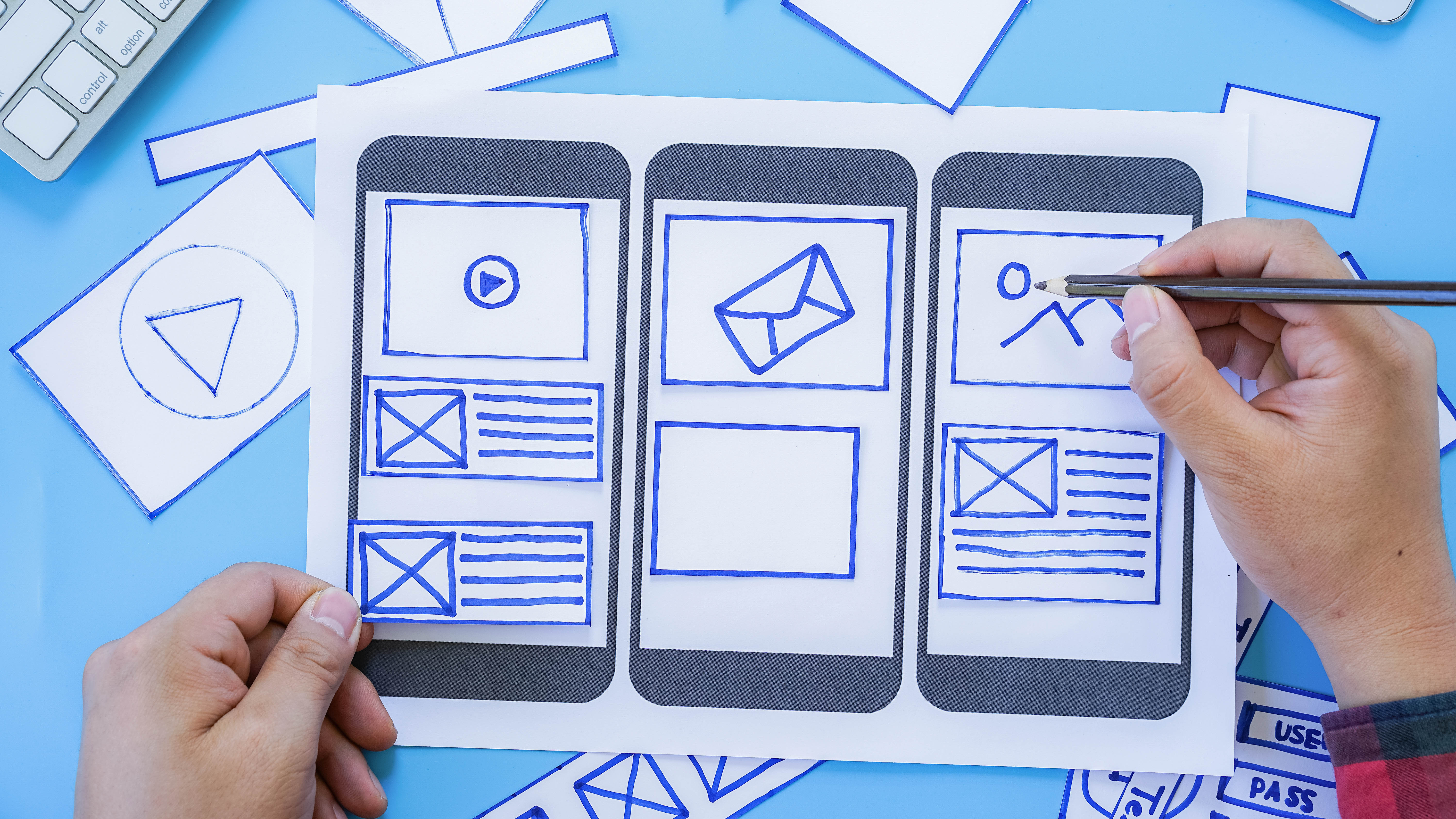 Hand, die einen Stift hält, zeichnet auf einem Papierprototypen für mobile App-Layouts, umgeben von weiteren Skizzen.