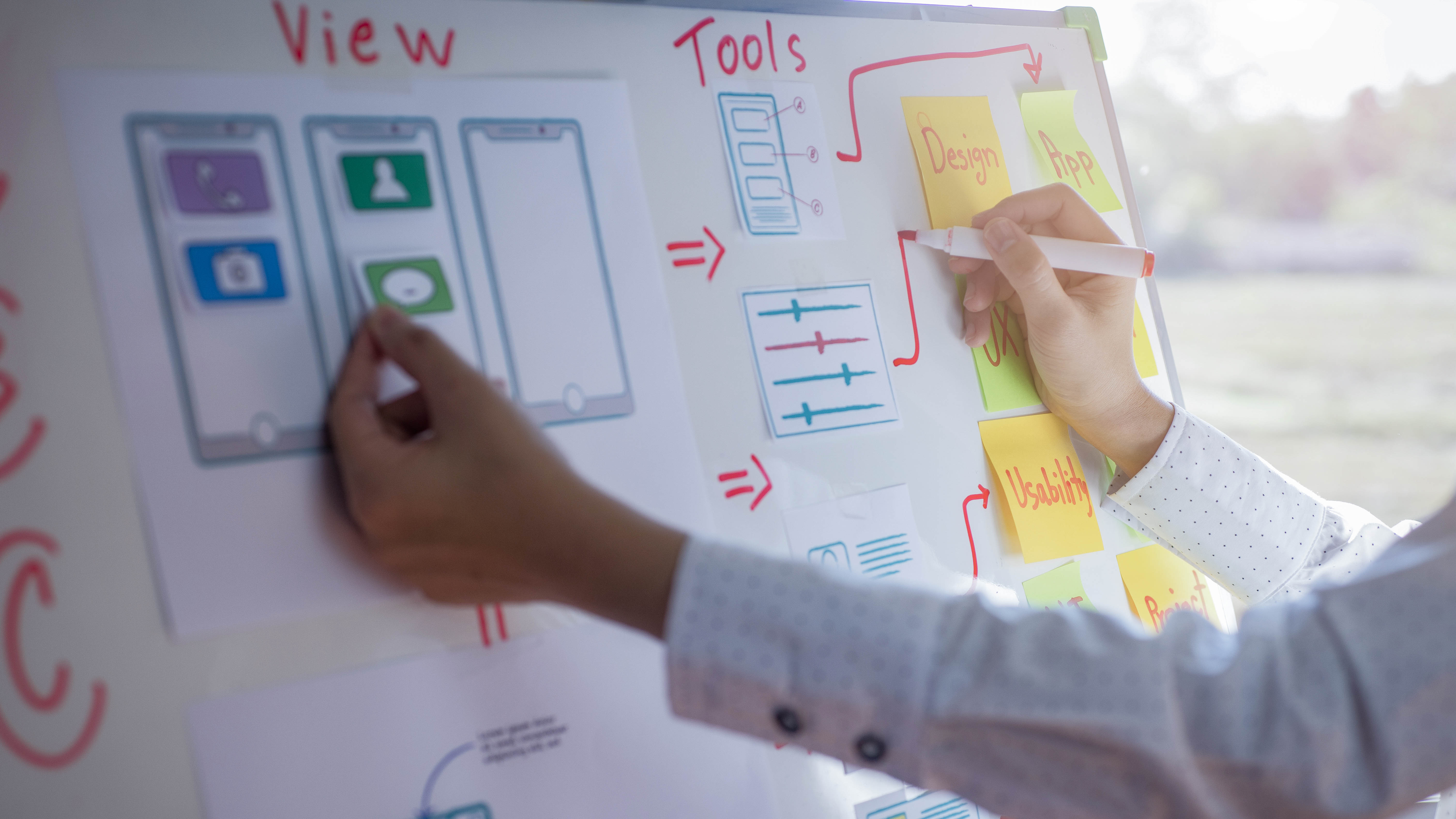 Hand, die ein Diagramm mit Smartphone-Illustrationen und Haftnotizen zum Thema Design und Tools bearbeitet.
