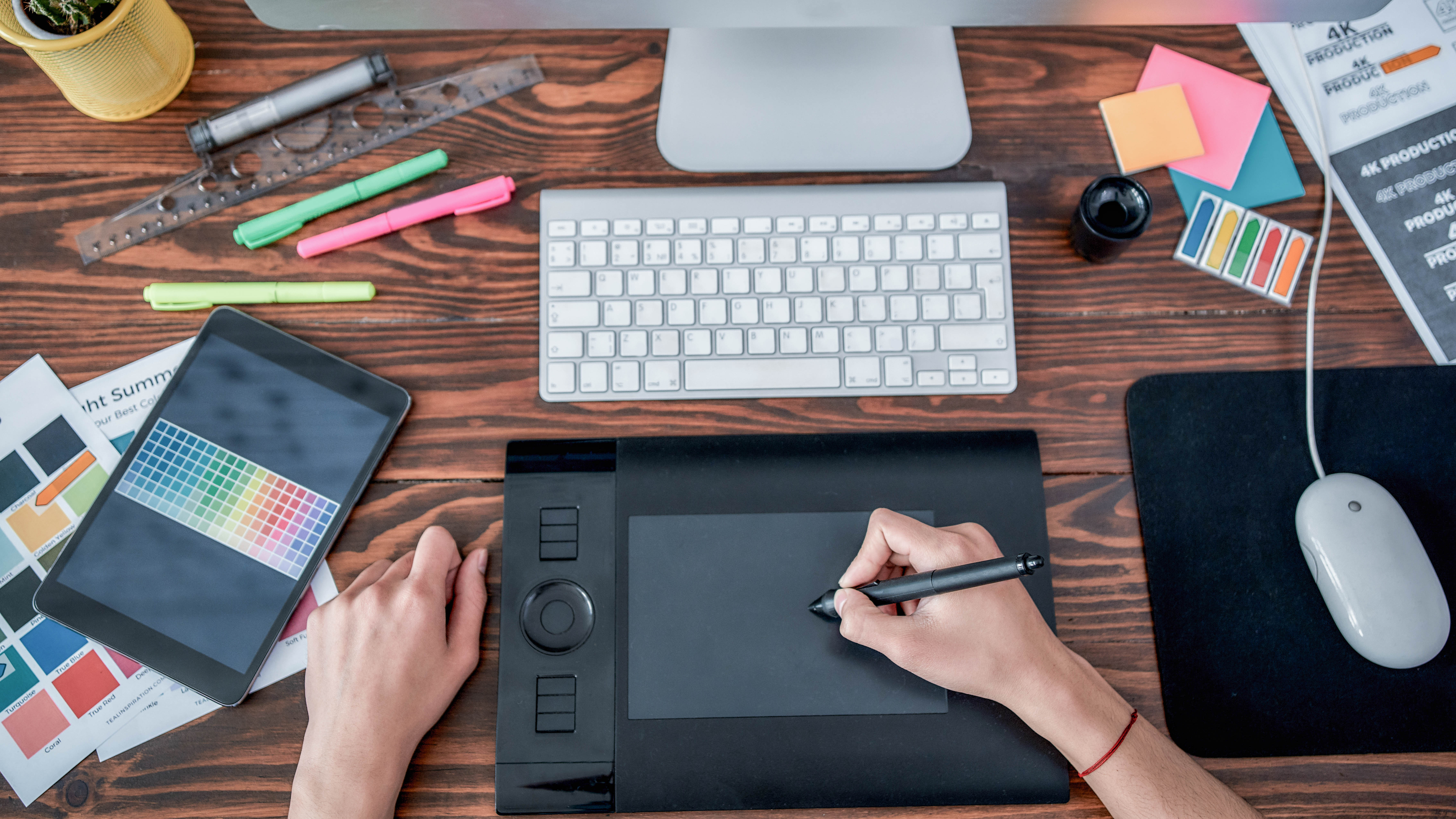 Ein Schreibtisch mit einem Grafiktablett, einer Tastatur, einem Tablet und verschiedenen Schreibutensilien.