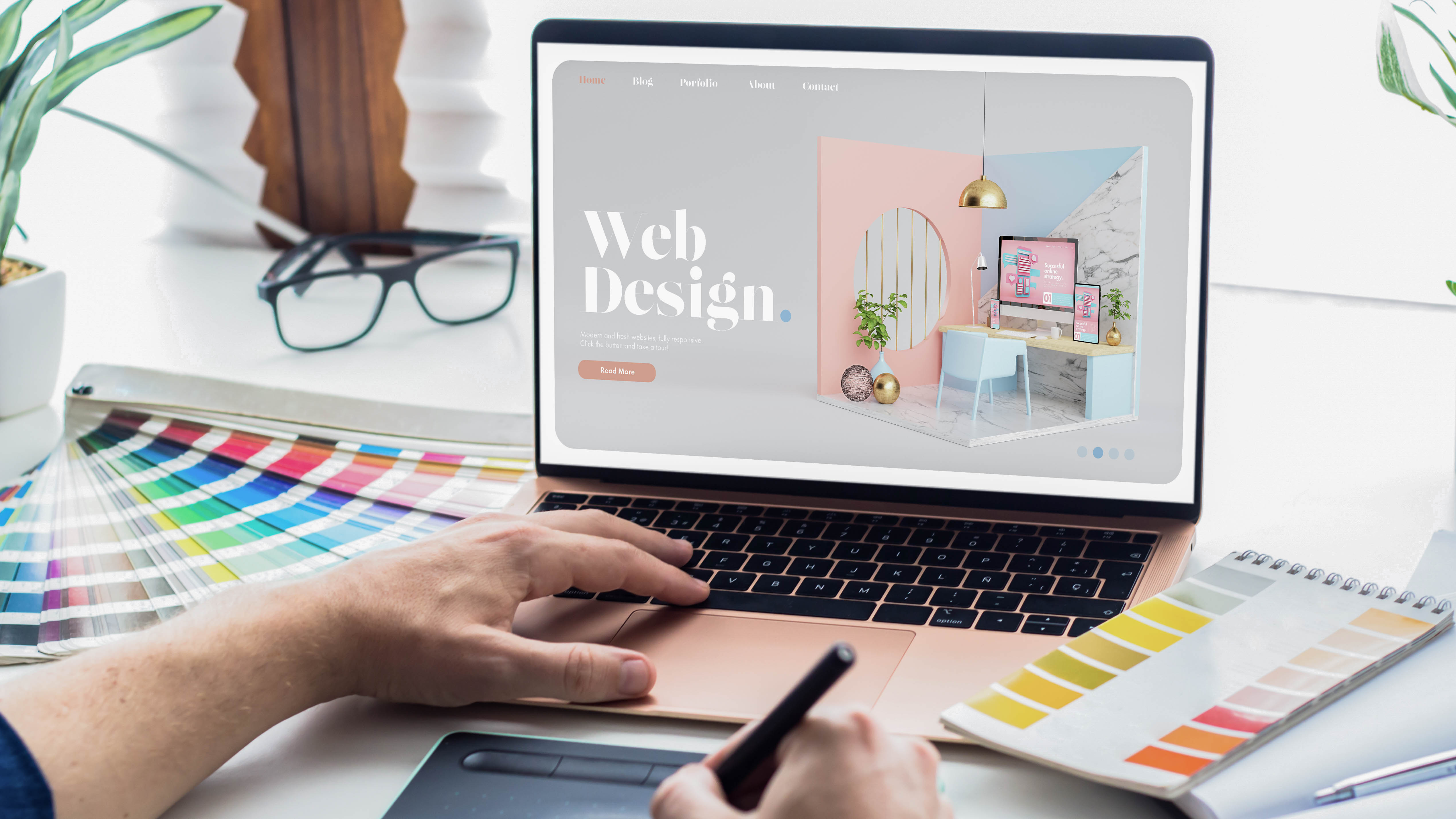 Laptop mit einer Webdesign-Website, daneben Farbmustertafeln und ein Notizblock.
