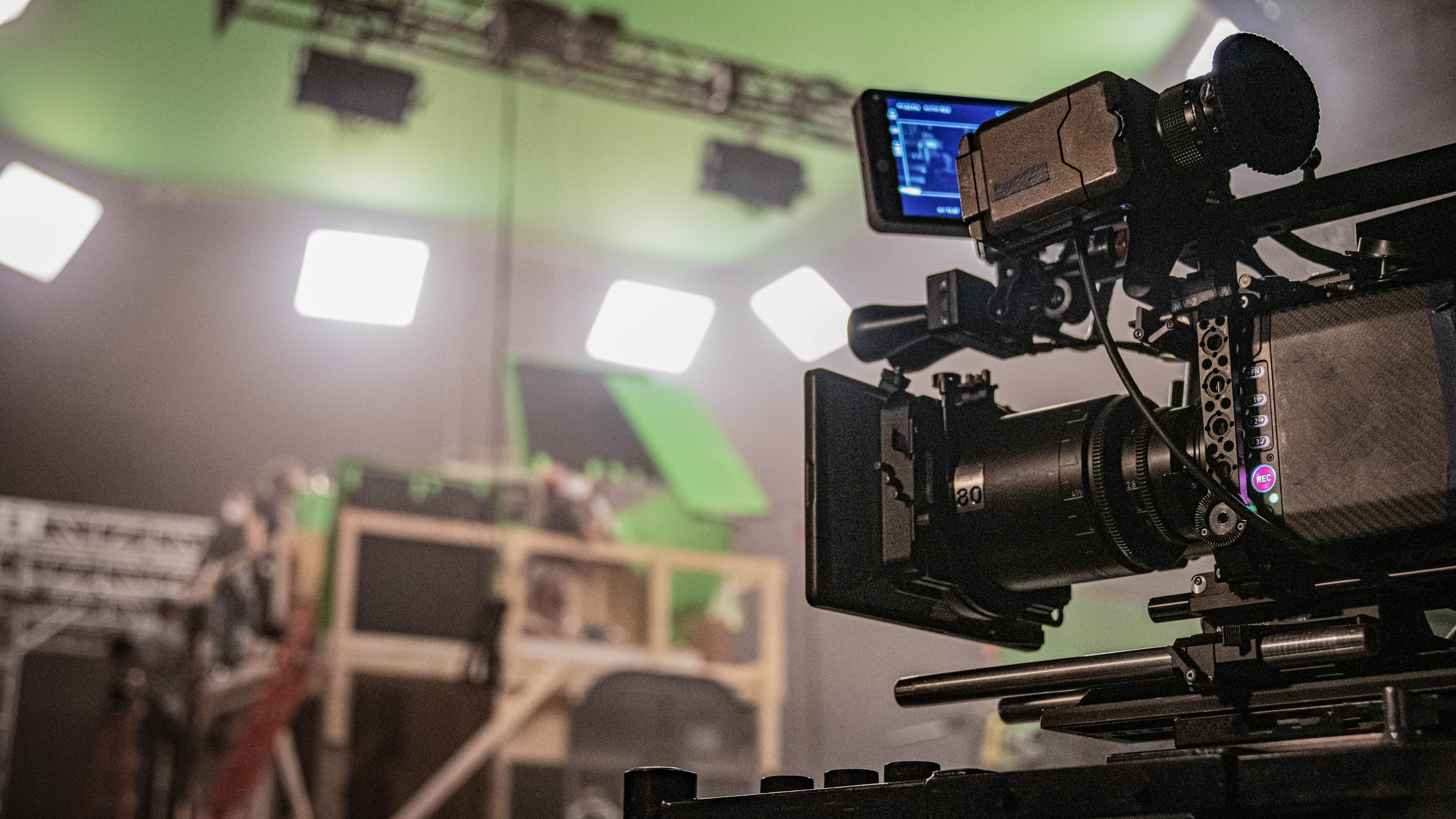 Kamera mit Monitor in einem Studio mit grüner Kulisse und mehreren Scheinwerfern im Hintergrund.
