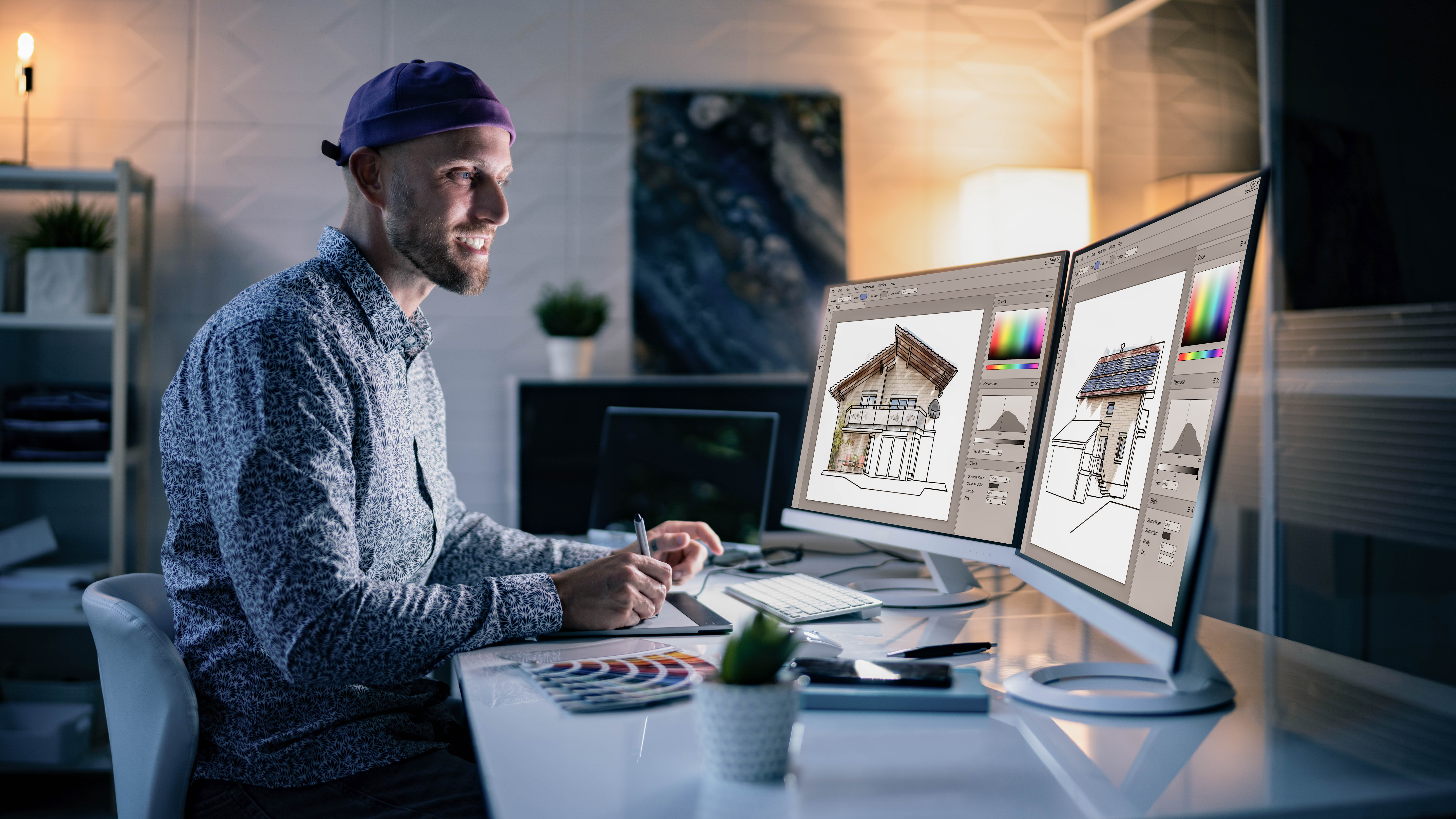 Ein Mann mit einer Mütze sitzt an einem Schreibtisch und arbeitet an zwei Monitoren mit Architekturzeichnungen.