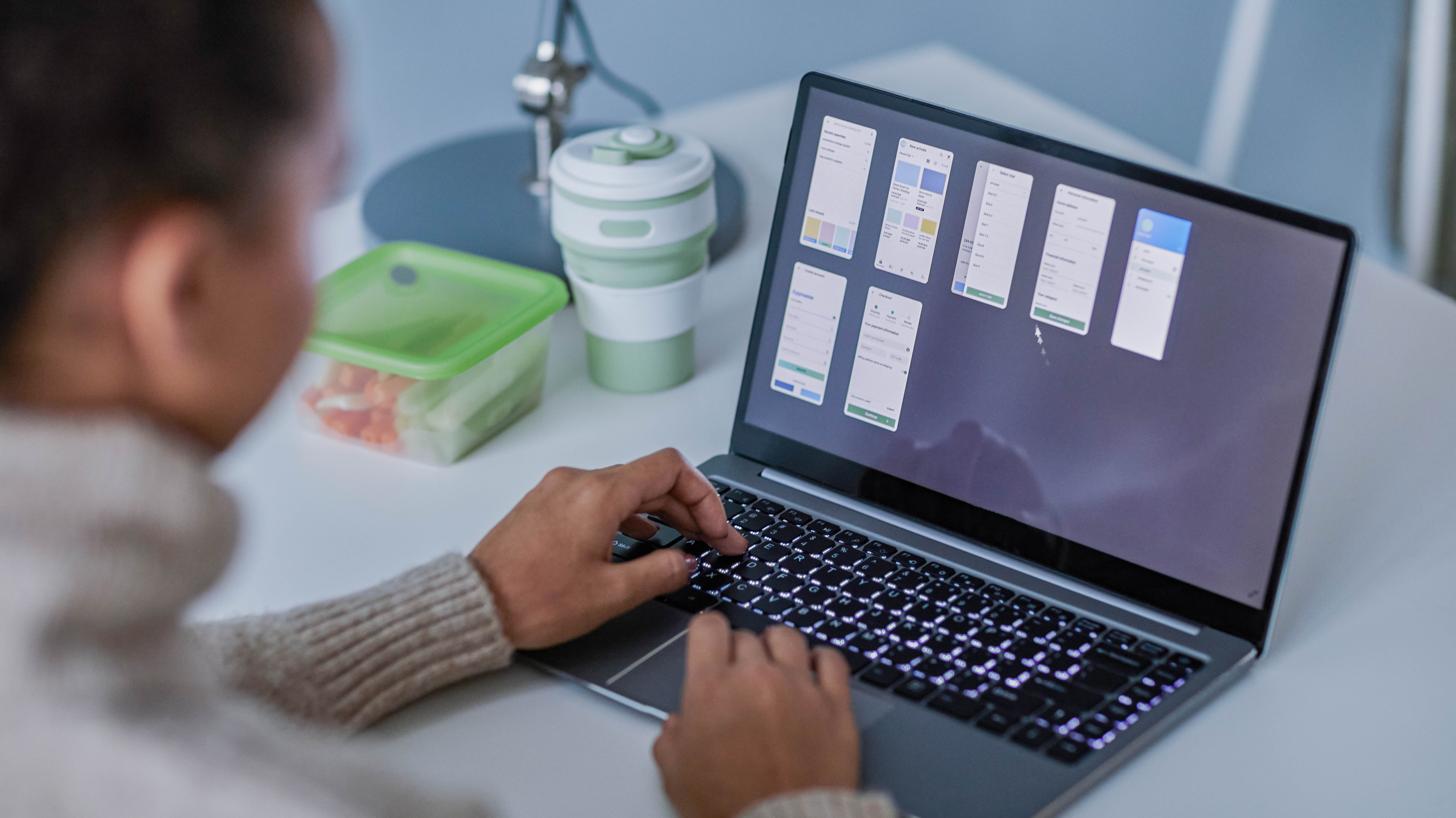 Eine Person arbeitet an einem Laptop, auf dem mehrere Bildschirmansichten von App-Designs angezeigt werden.