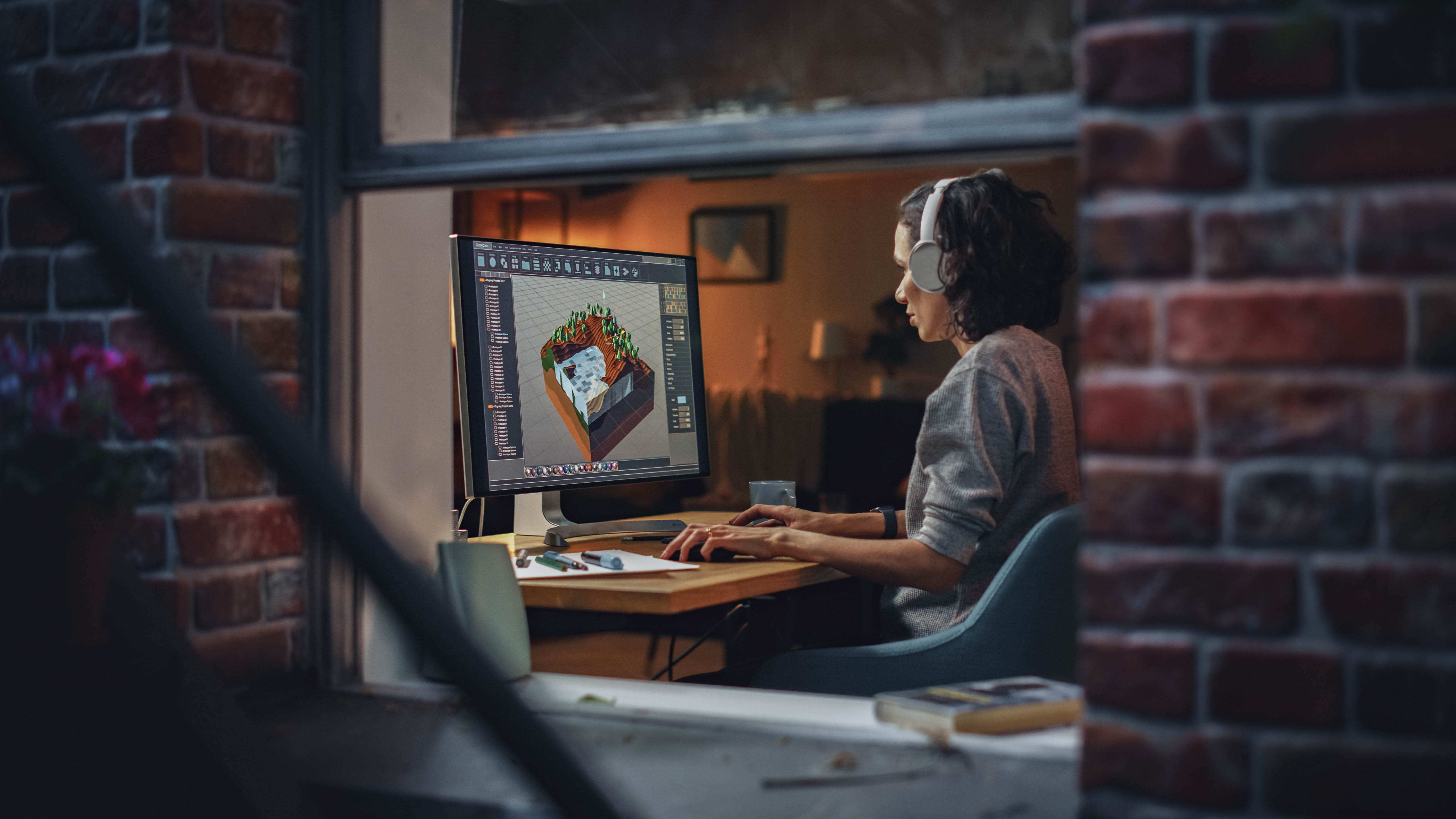 Eine Person mit Kopfhörern arbeitet an einem Computer, der ein 3D-Modell zeigt, in einem gemütlichen Raum.