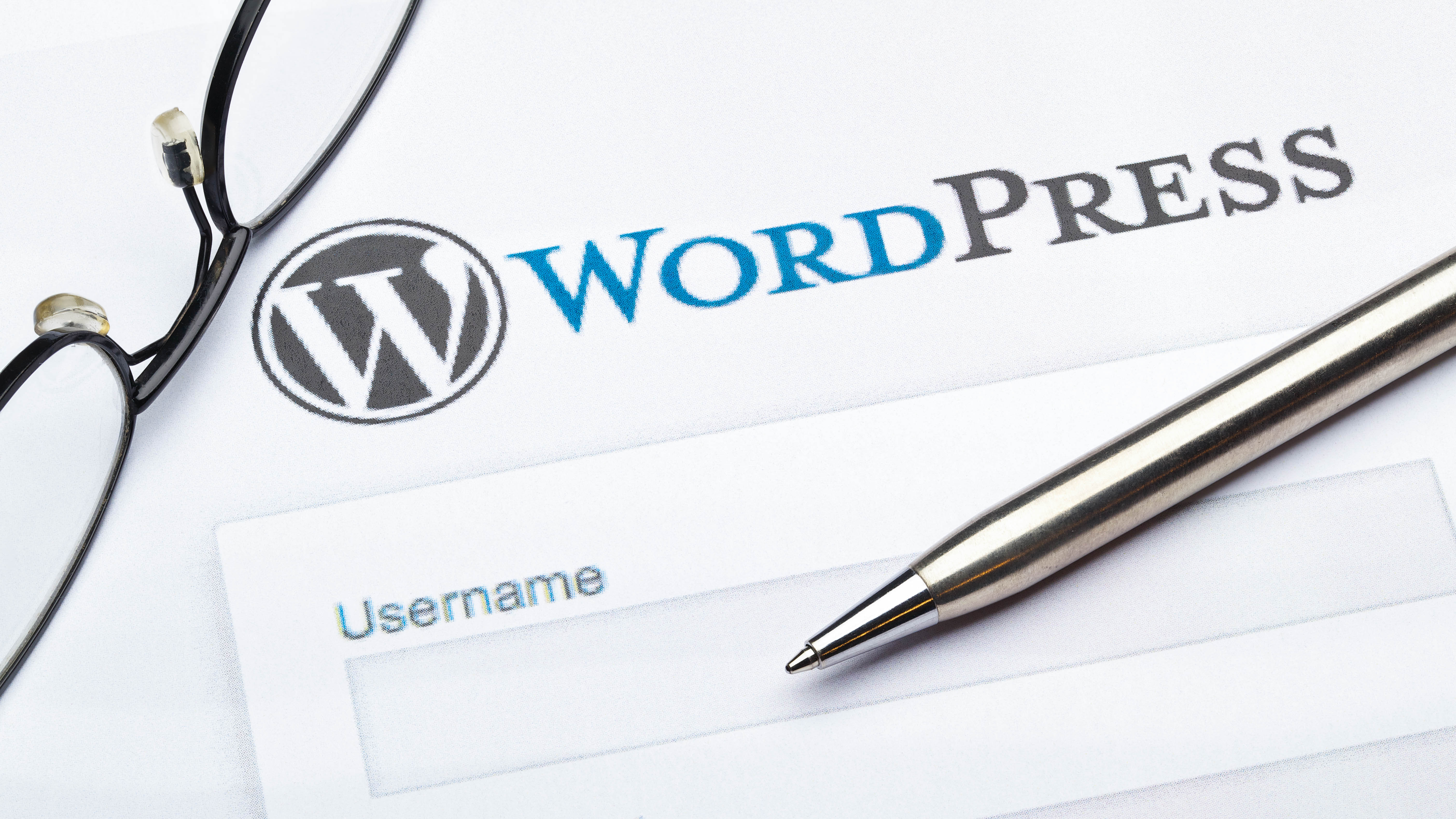 Brille und Kugelschreiber liegen neben einem WordPress-Anmeldeformular mit dem Feld für den Benutzernamen.