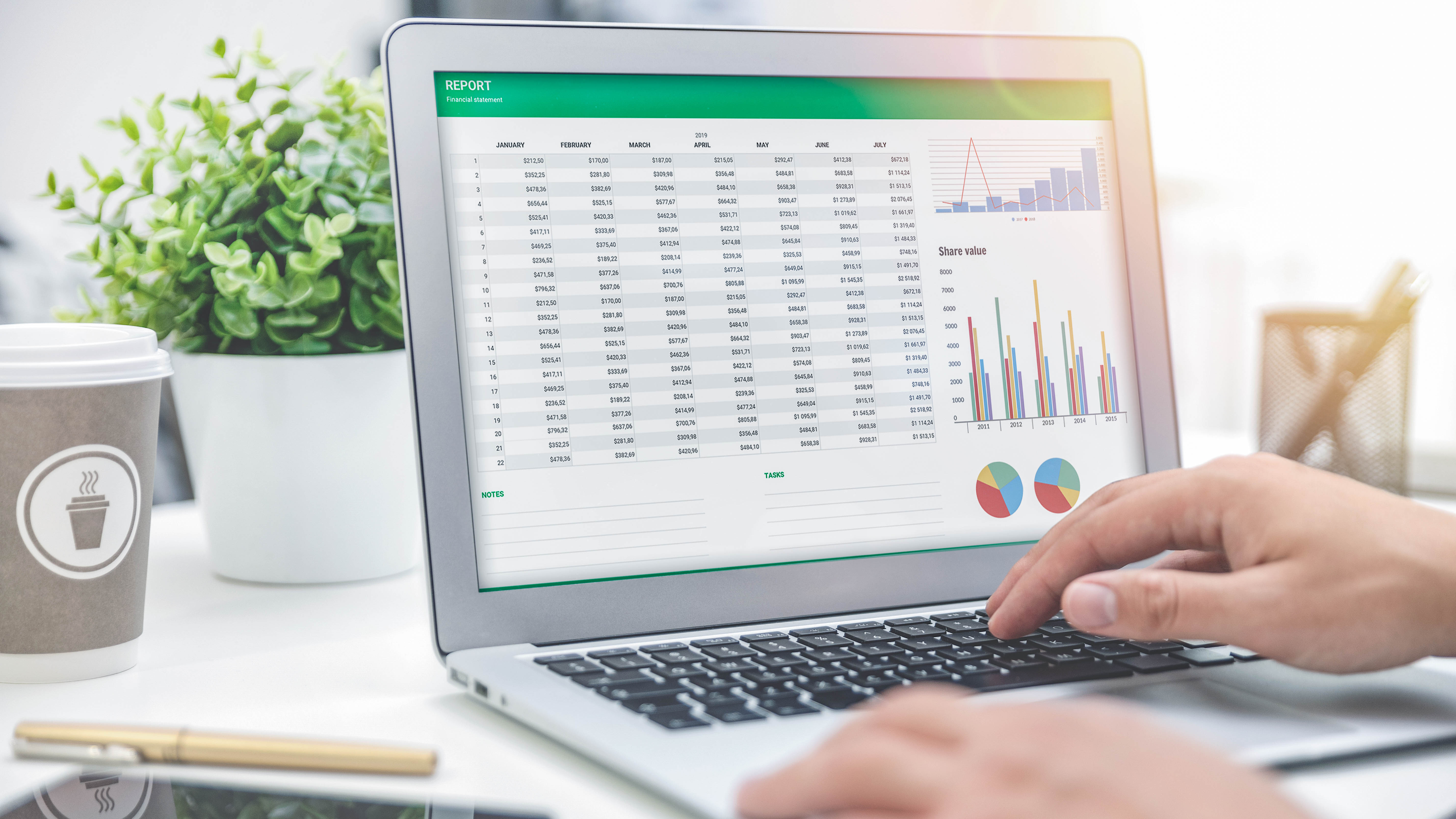 Ein Laptop zeigt eine Finanzübersicht mit Tabellen und Diagrammen, daneben eine Kaffeetasse und eine Pflanze.