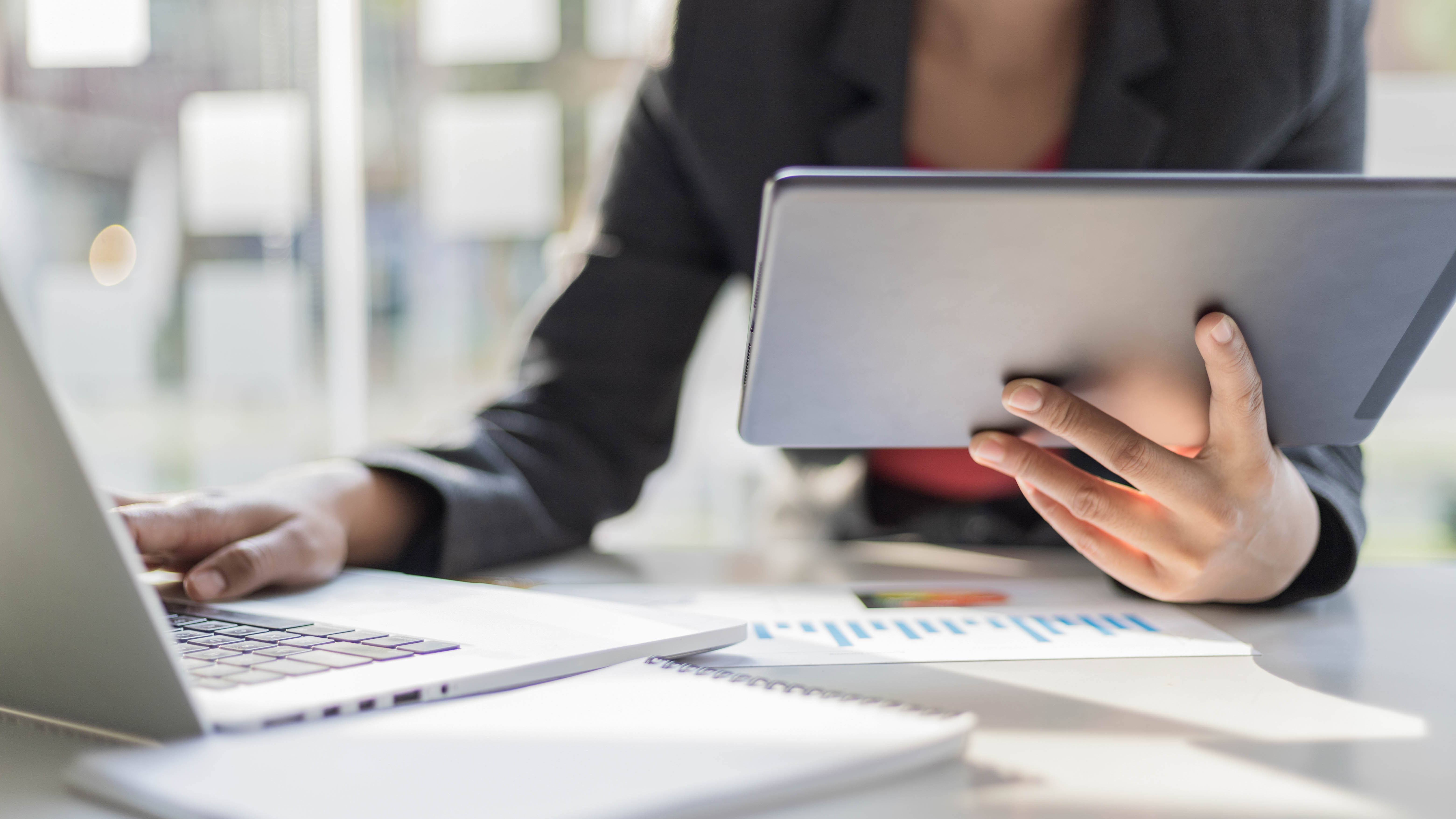 Eine Person hält ein Tablet in der Hand, während sie an einem Laptop arbeitet, umgeben von Notizen und Diagrammen.