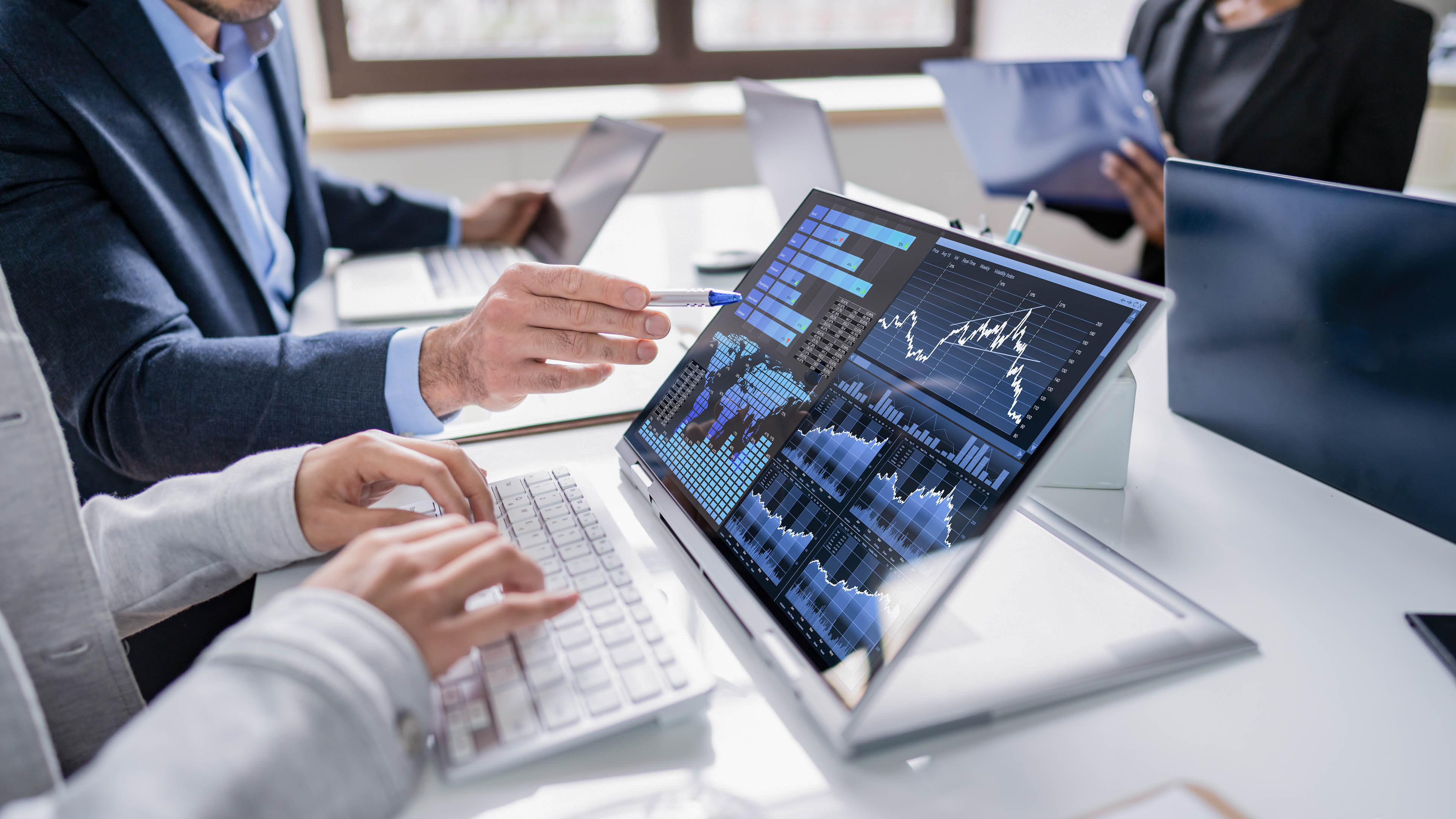 Personen analysieren Daten auf einem Laptop mit Grafiken und Diagrammen in einem modernen Büro.