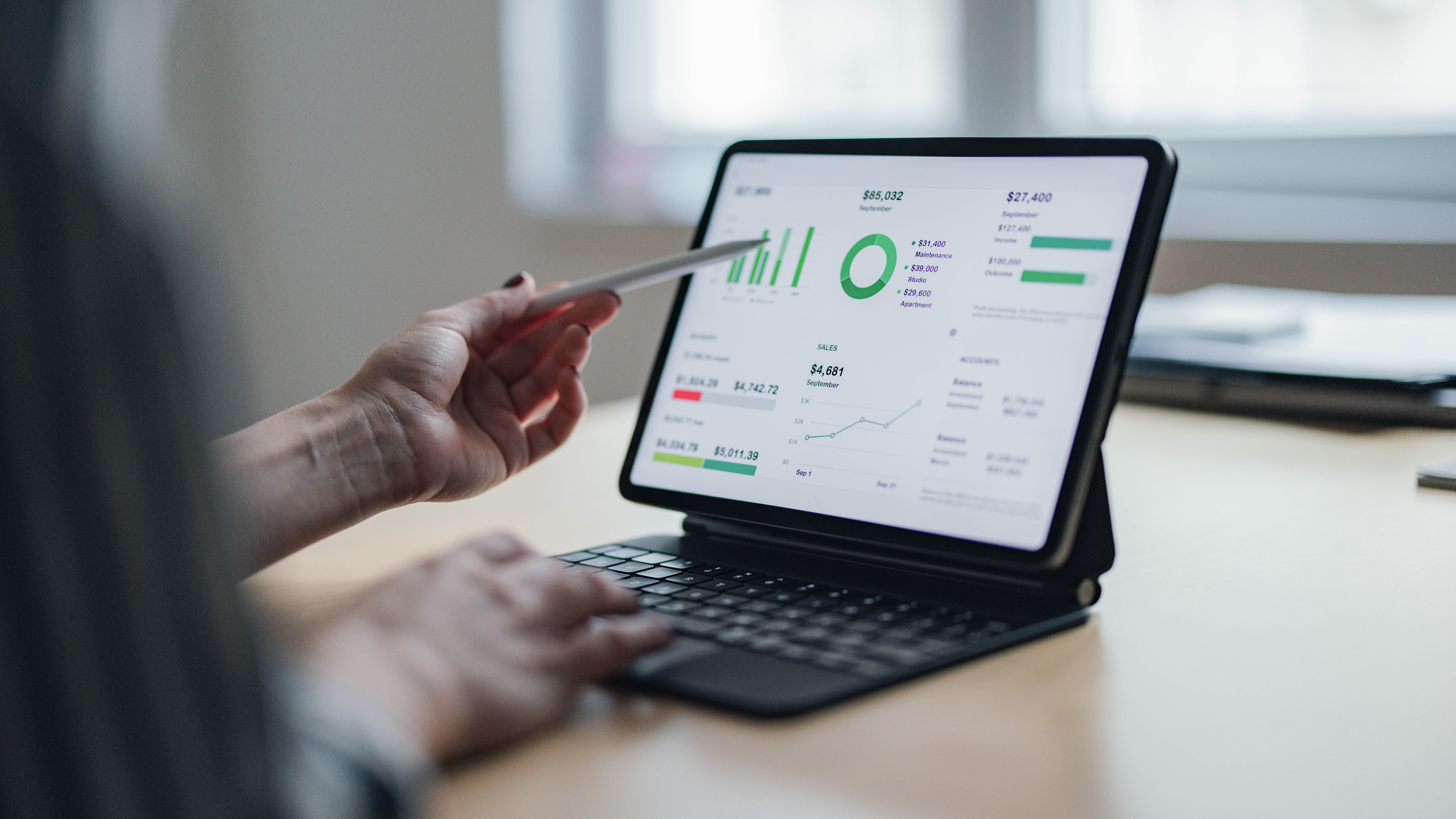 Eine Hand hält einen Stift und zeigt auf ein Tablet mit Finanzdaten und Diagrammen.
