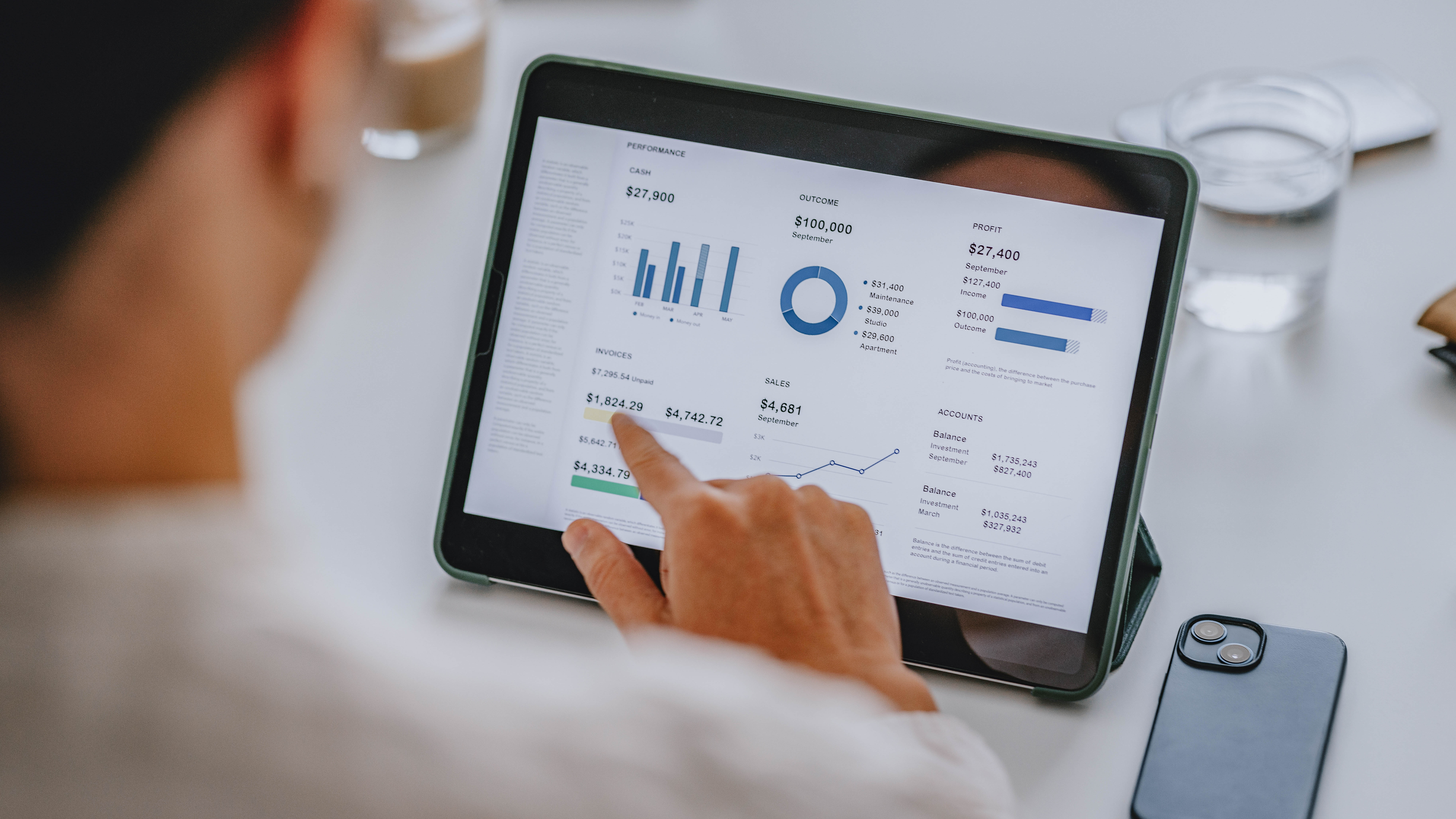 Eine Hand zeigt auf ein Tablet mit Finanzdaten, Diagrammen und Statistiken.