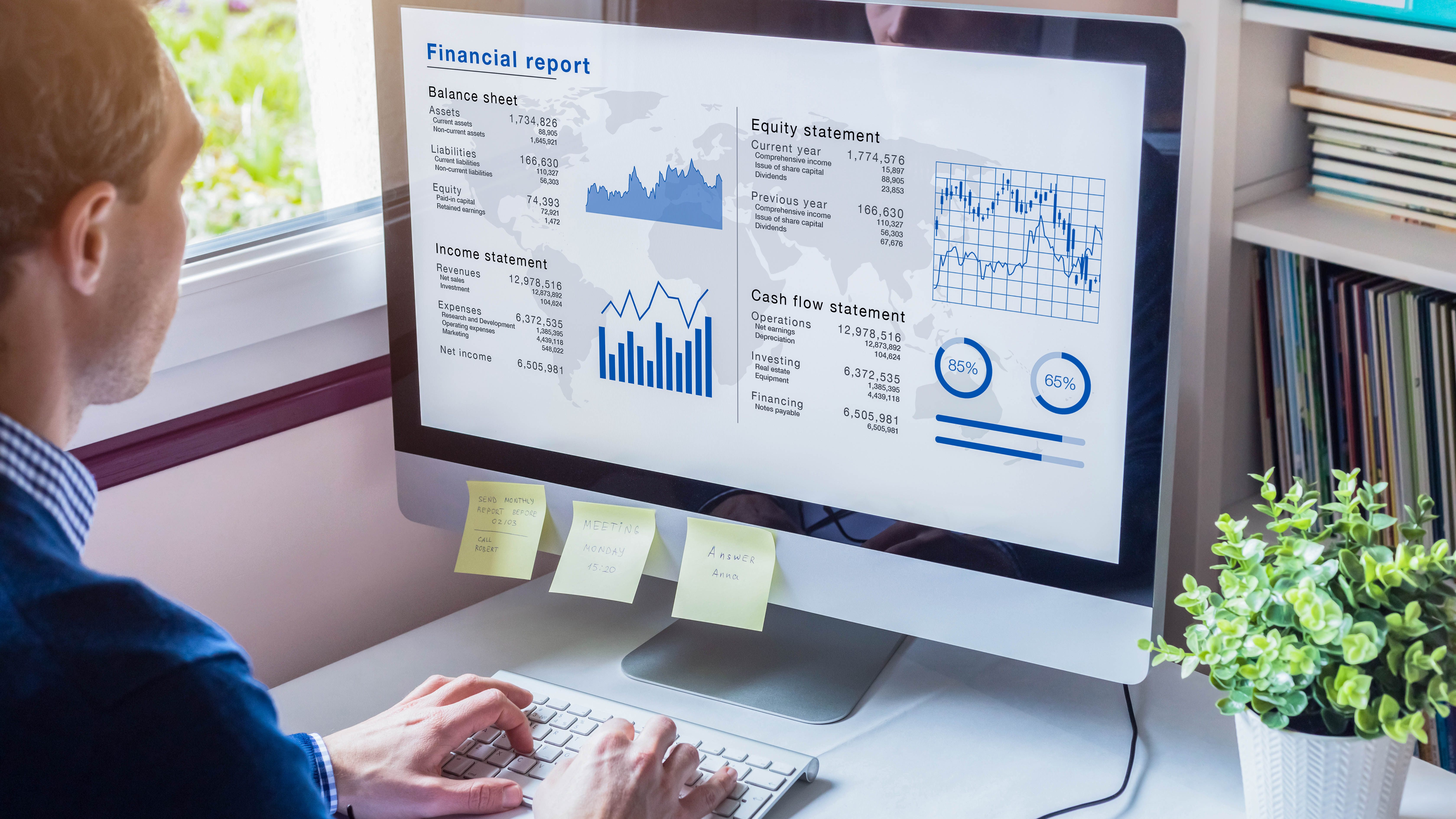 Mann betrachtet einen Computerbildschirm mit einem Finanzbericht und Diagrammen, Post-its sind auf dem Monitor befestigt.