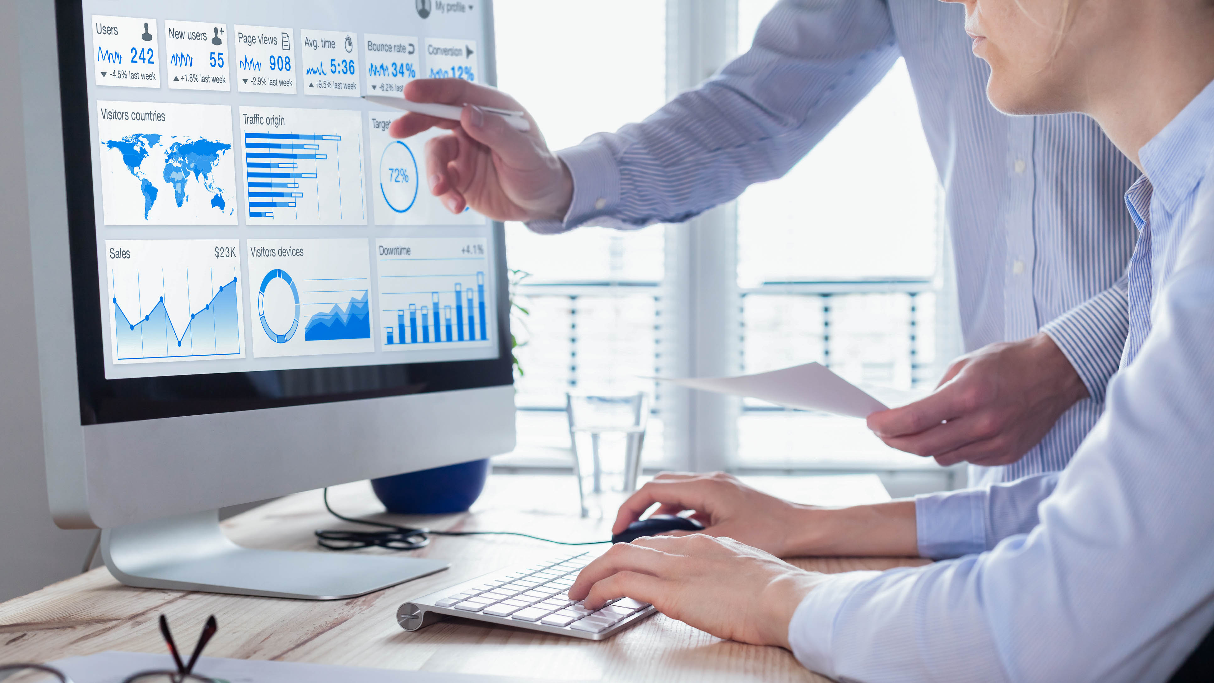 Zwei Personen analysieren Daten auf einem Computerbildschirm mit Diagrammen und Statistiken.