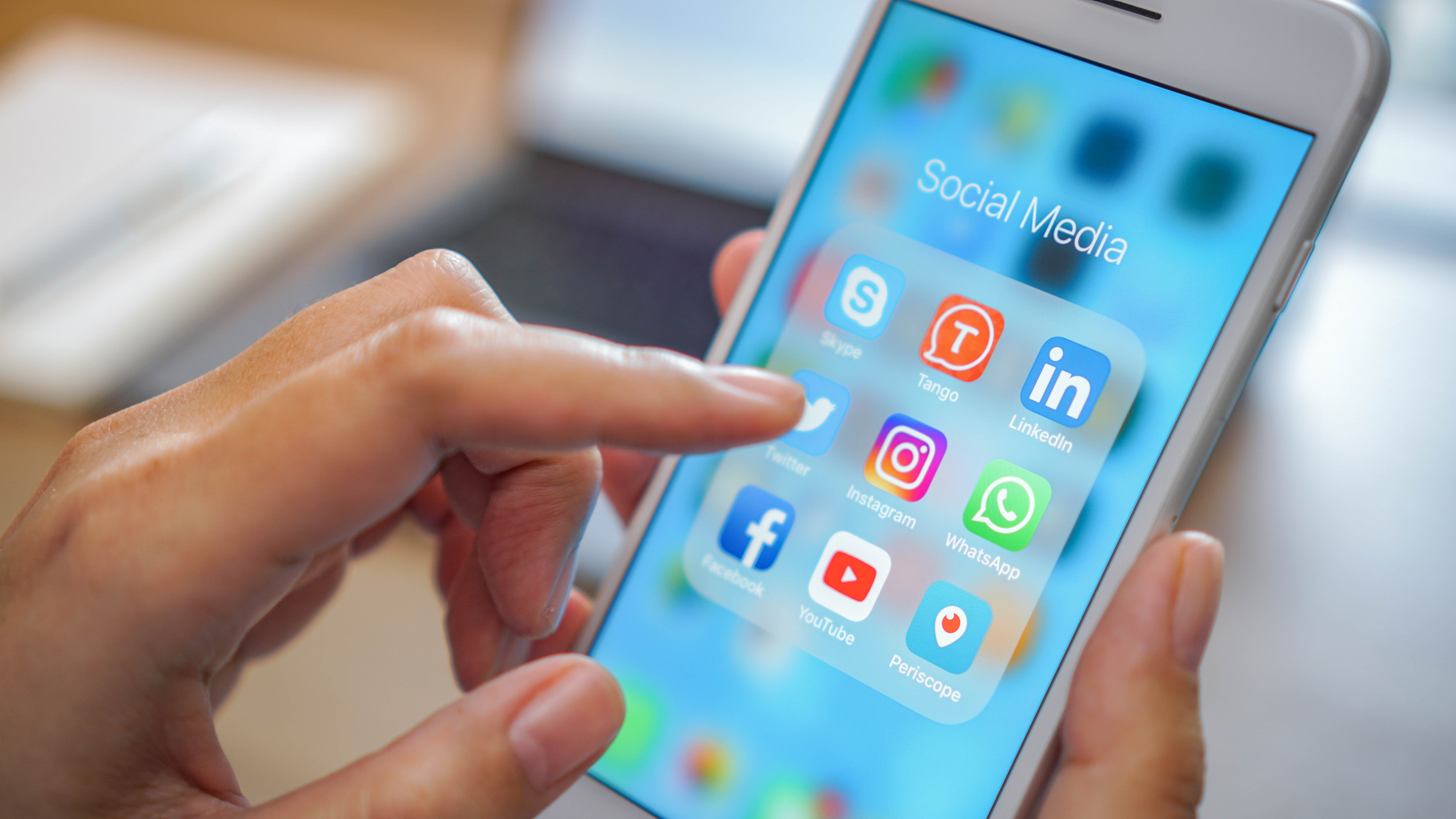 Hand mit Finger, der auf ein Smartphone-Display mit Social-Media-Apps tippt.