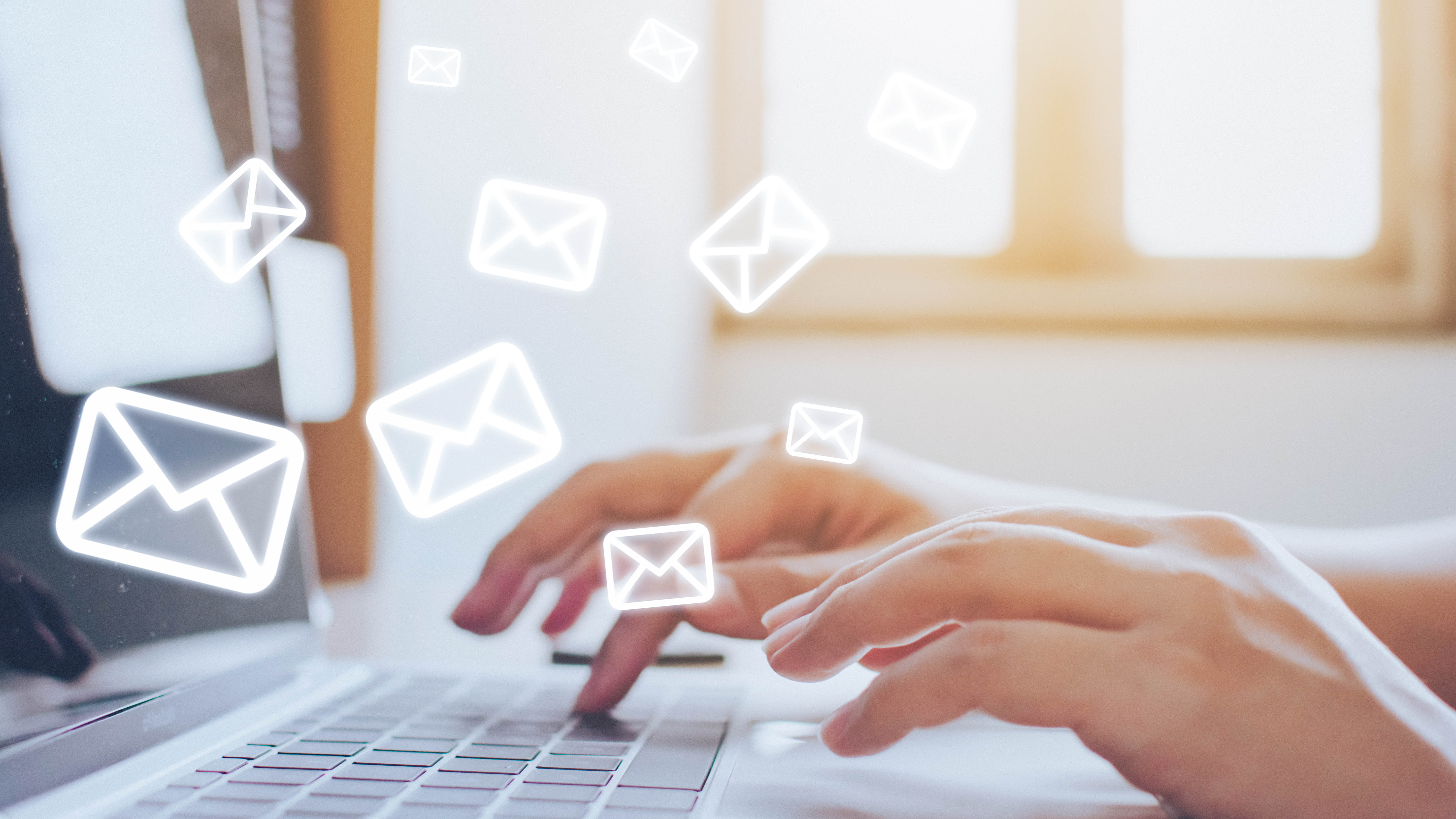 Hände tippen auf einer Laptop-Tastatur, umgeben von grafischen E-Mail-Symbolen.
