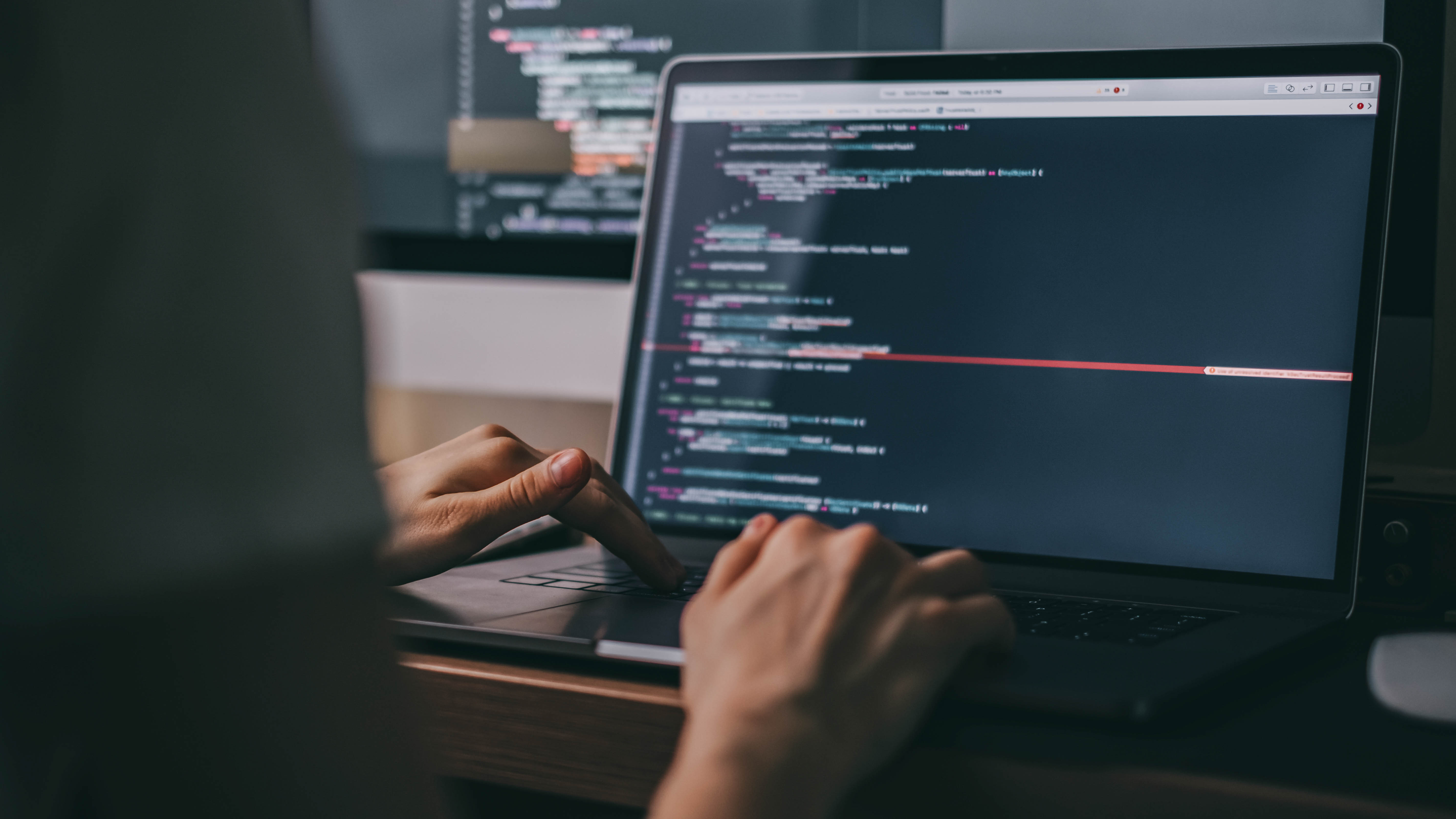 Hände tippen auf einer Laptop-Tastatur, während Code auf dem Bildschirm angezeigt wird.