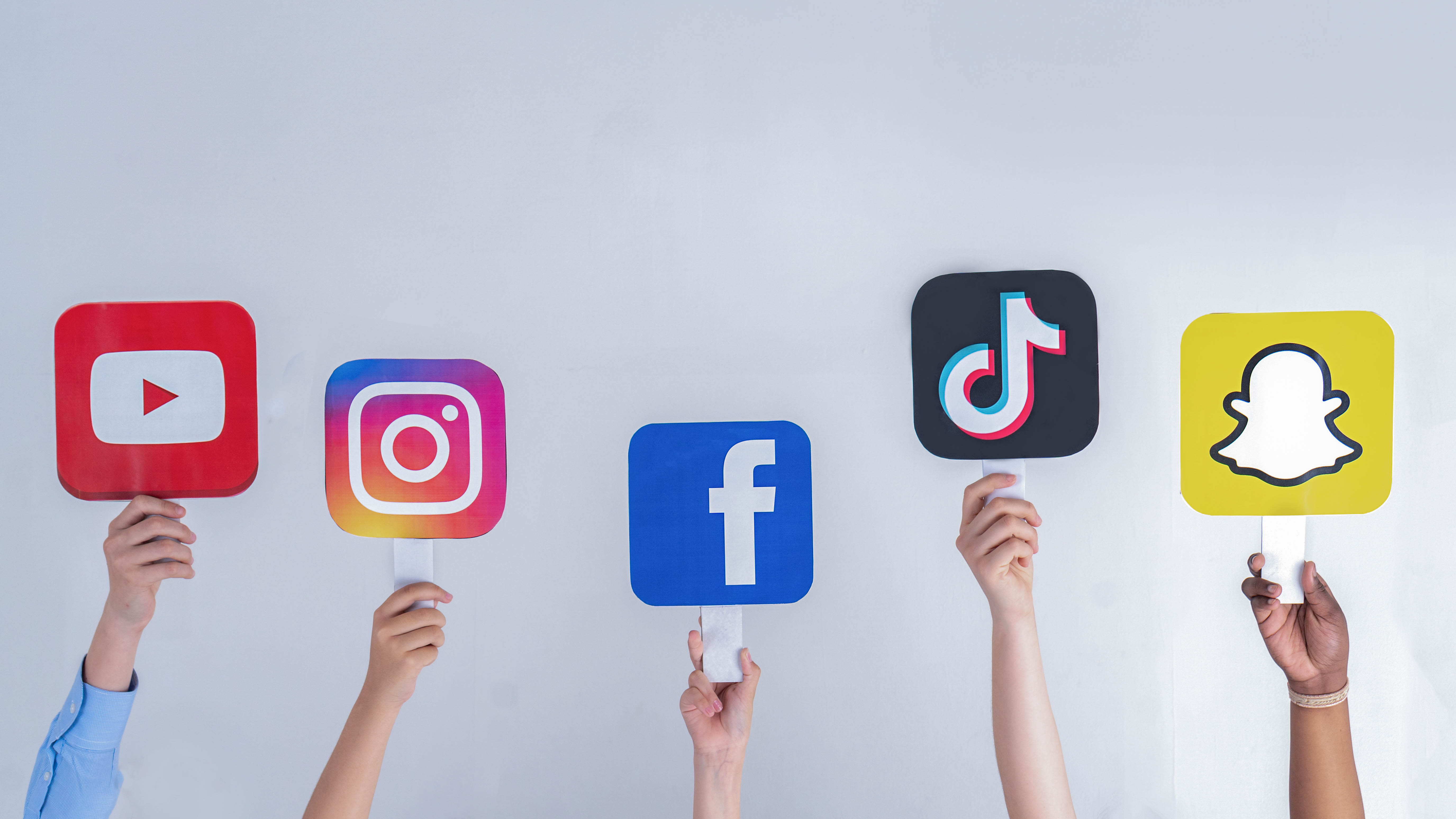 Hände halten große Schilder mit den Logos von YouTube, Instagram, Facebook, TikTok und Snapchat.