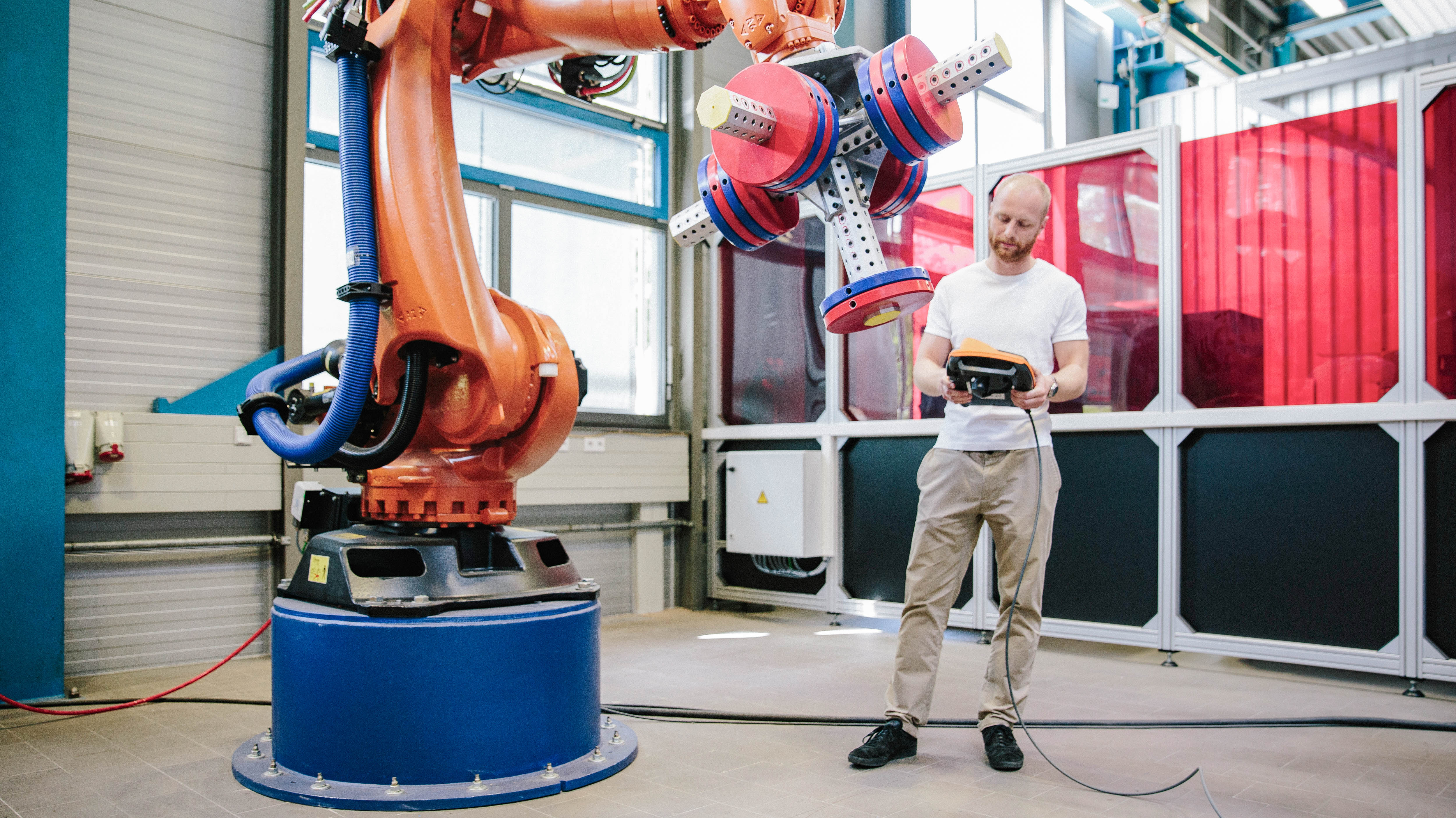 Ein Mensch steht vor einem Industrieroboter und hält ein Steuergerät in der Hand.