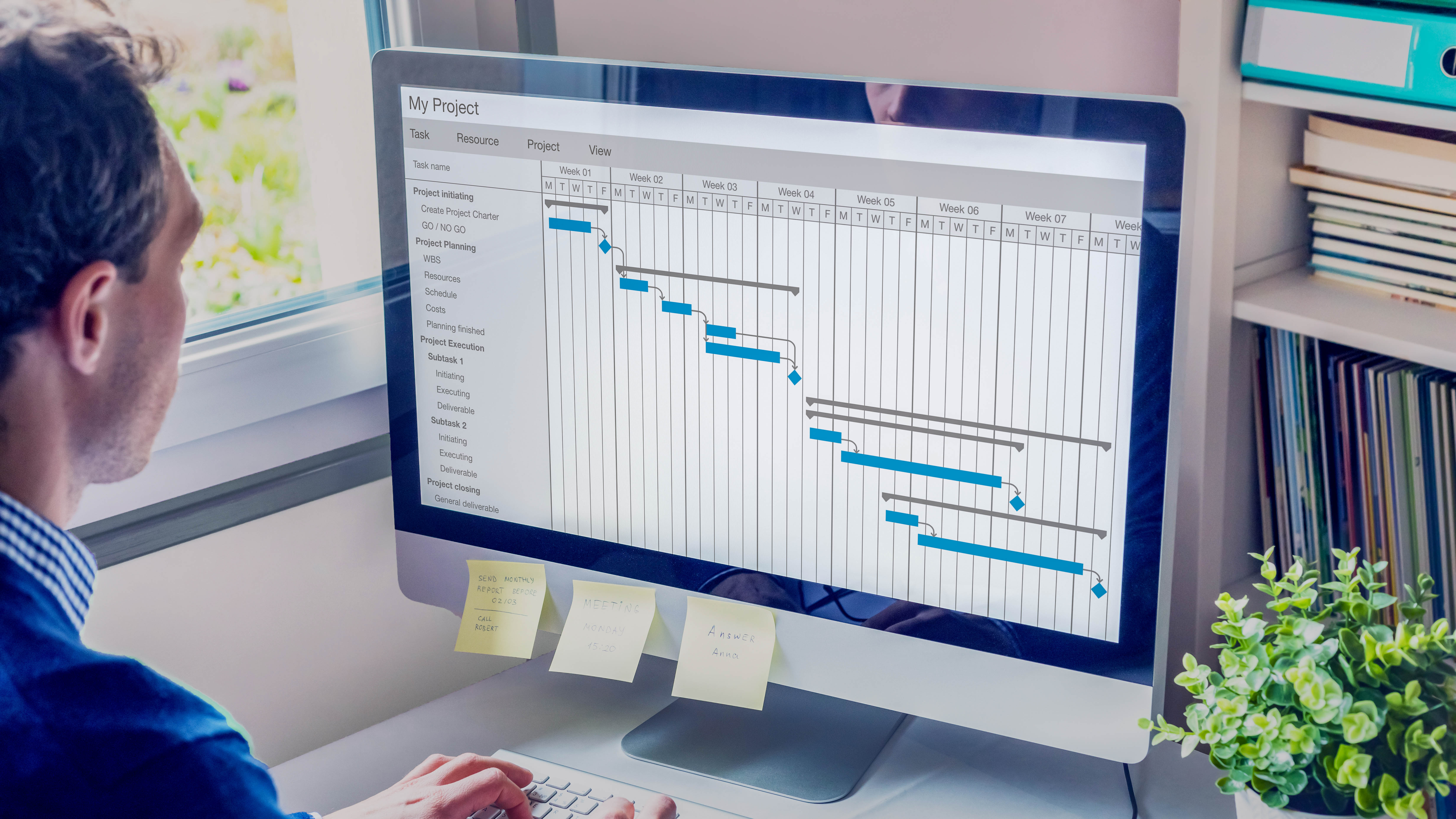 Ein Mann sitzt vor einem Computer, auf dem ein Gantt-Diagramm für Projektmanagement angezeigt wird.