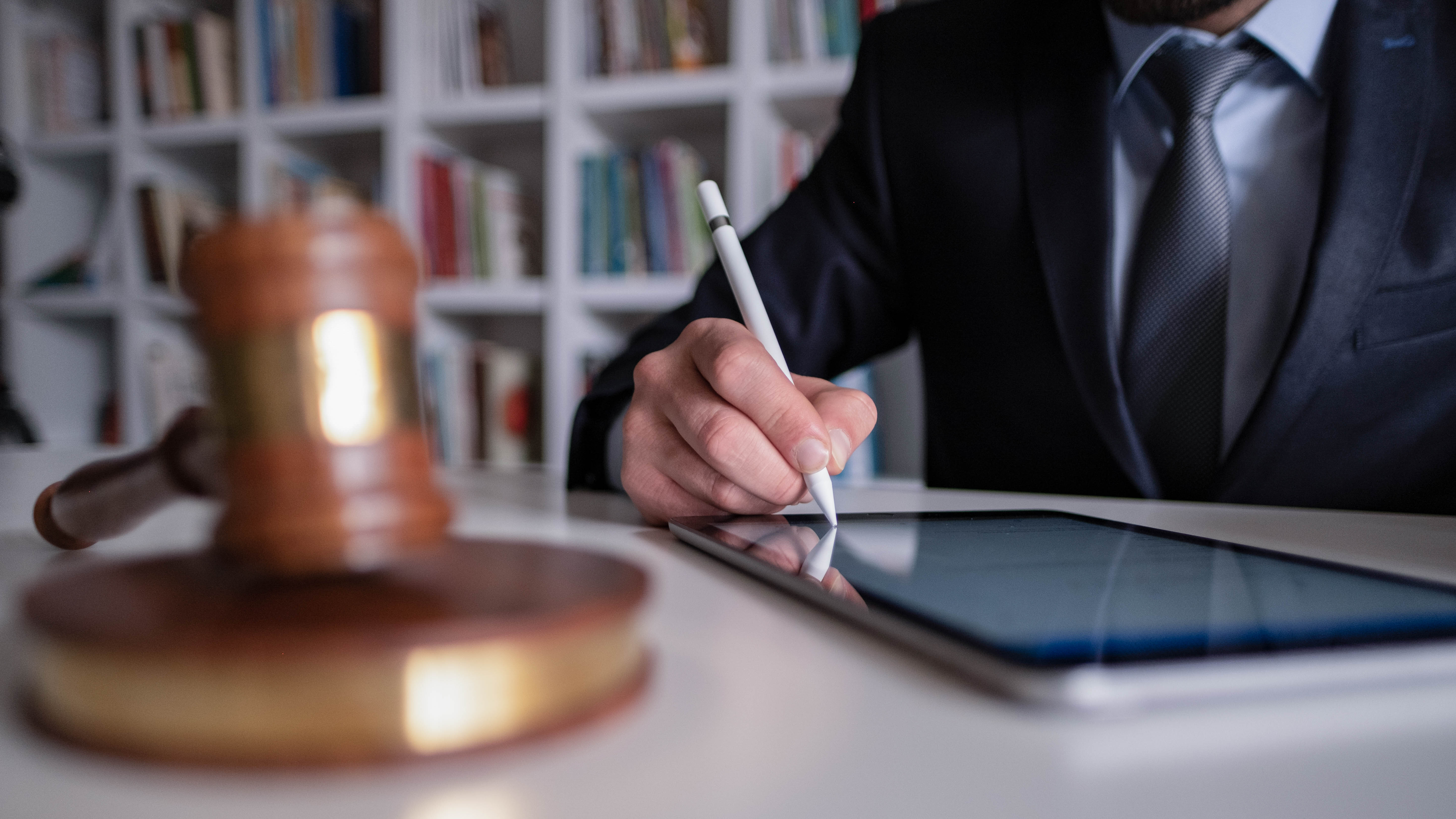 Ein Mann in Anzug schreibt mit einem Stylus auf einem Tablet, während ein Richterhammer im Vordergrund liegt.
