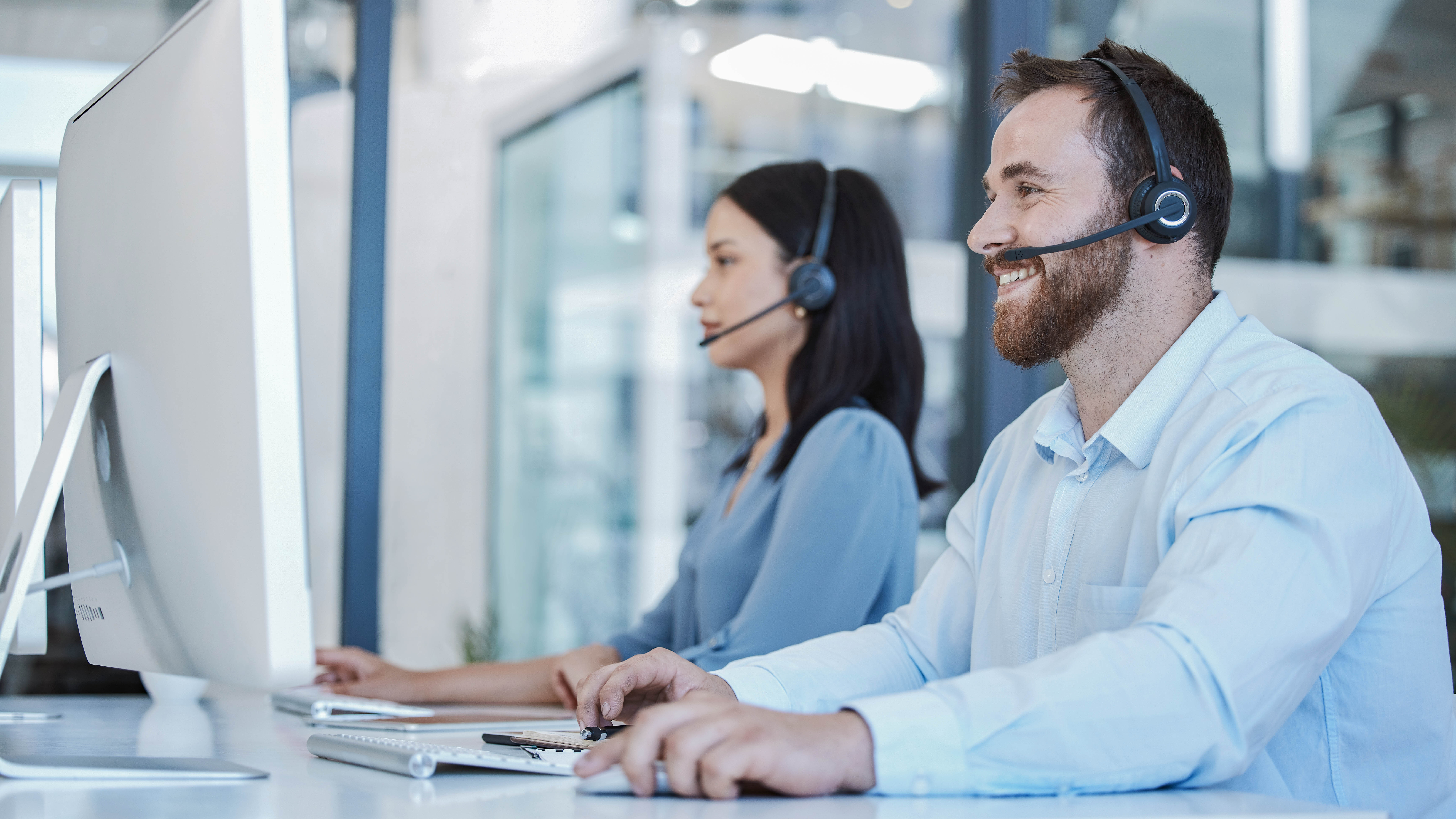 Zwei Personen mit Headsets arbeiten an Computern in einem modernen Büro.