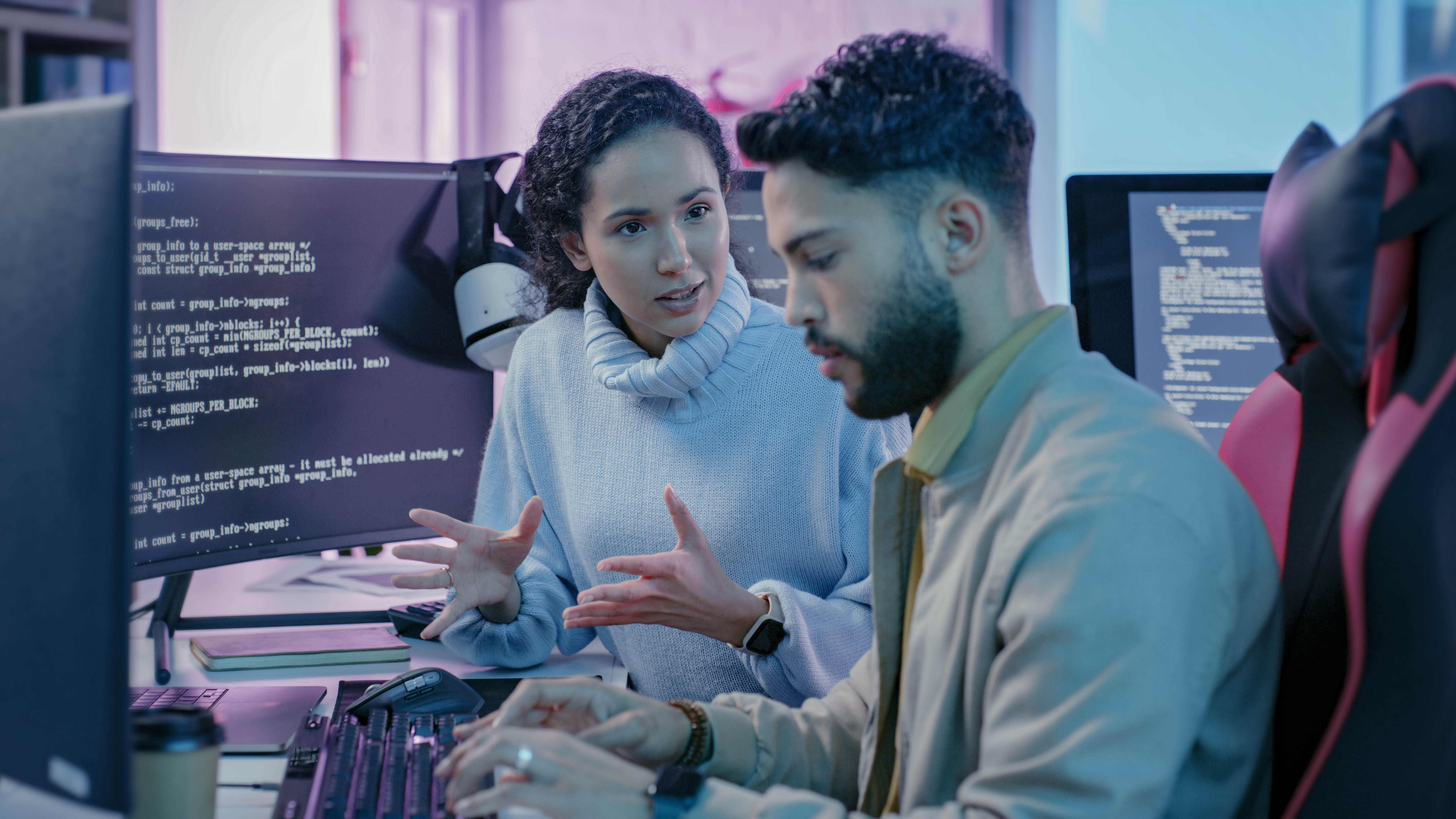 Zwei Personen diskutieren an einem Computer, während Code auf dem Bildschirm angezeigt wird.