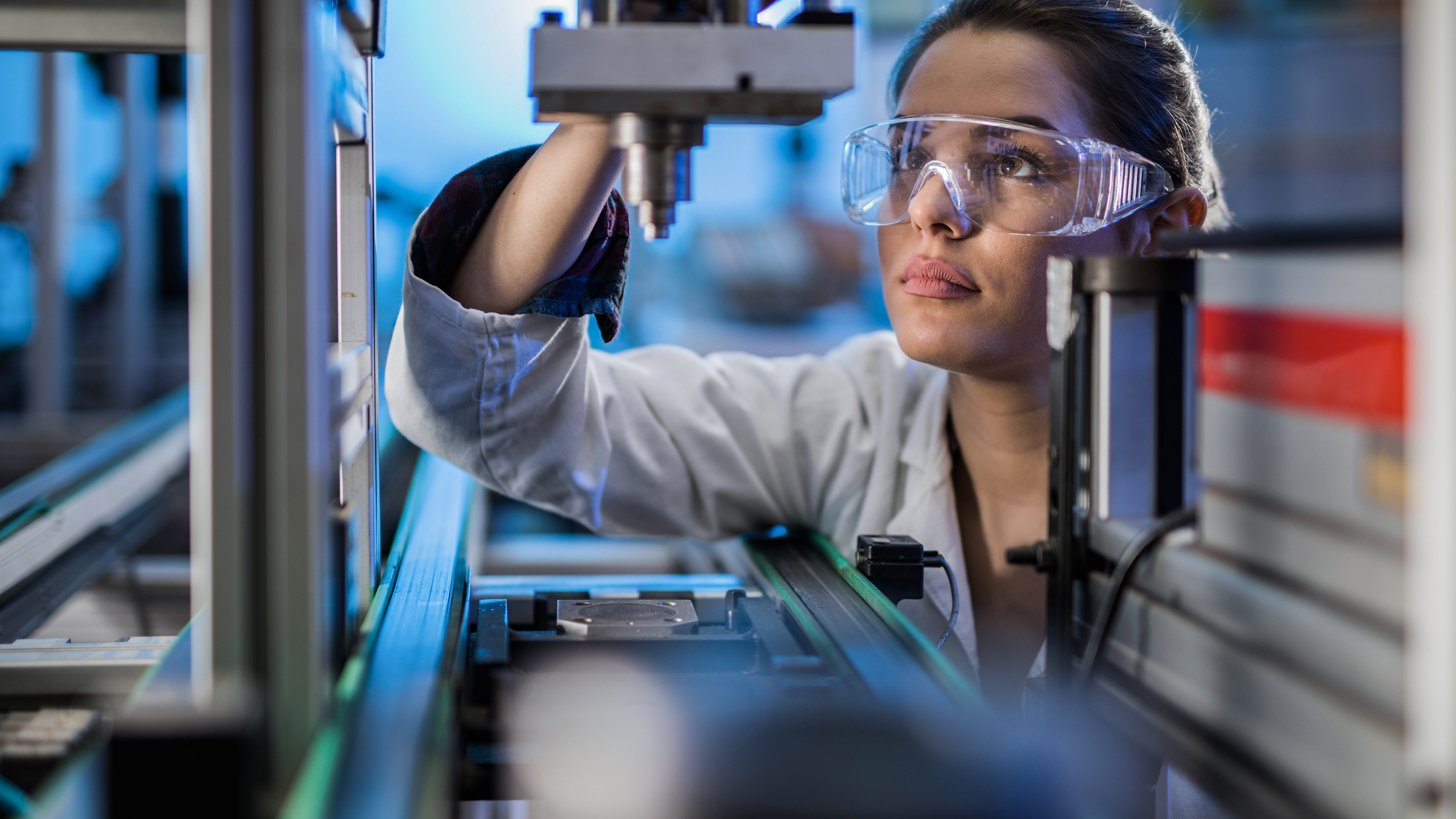 Eine Person in Schutzbrille und Laborkittel arbeitet konzentriert an einer technischen Maschine.