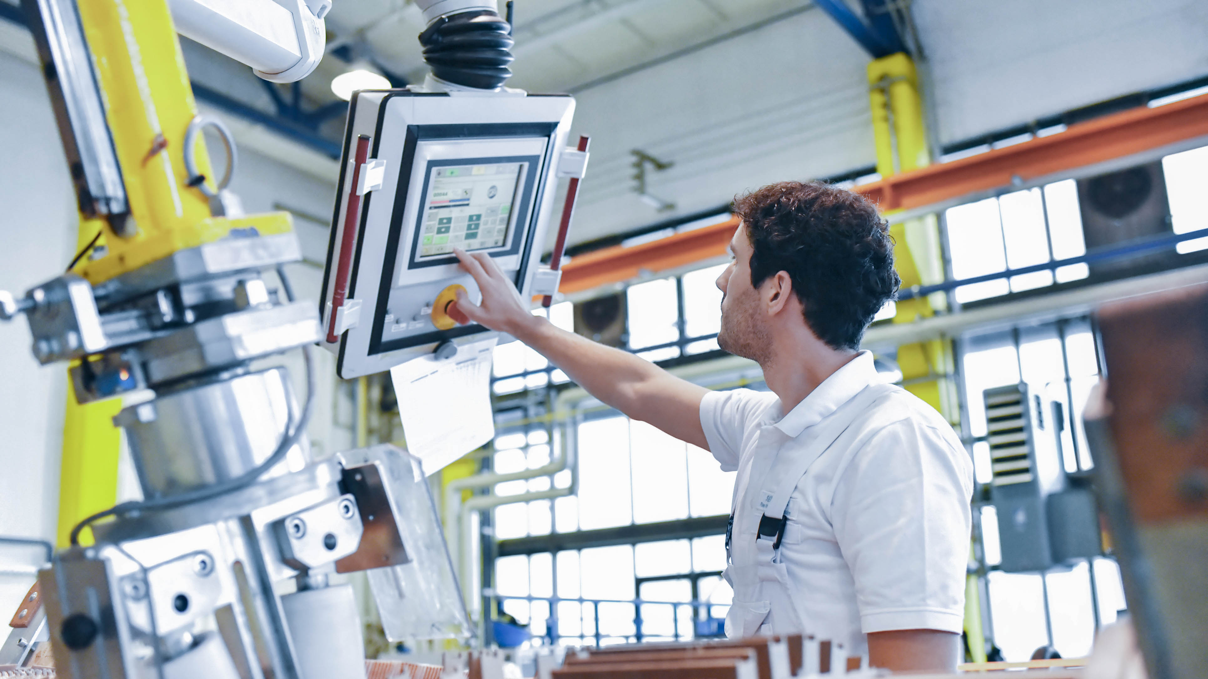 Ein Arbeiter bedient ein digitales Steuerpanel in einer modernen Fabrikhalle.