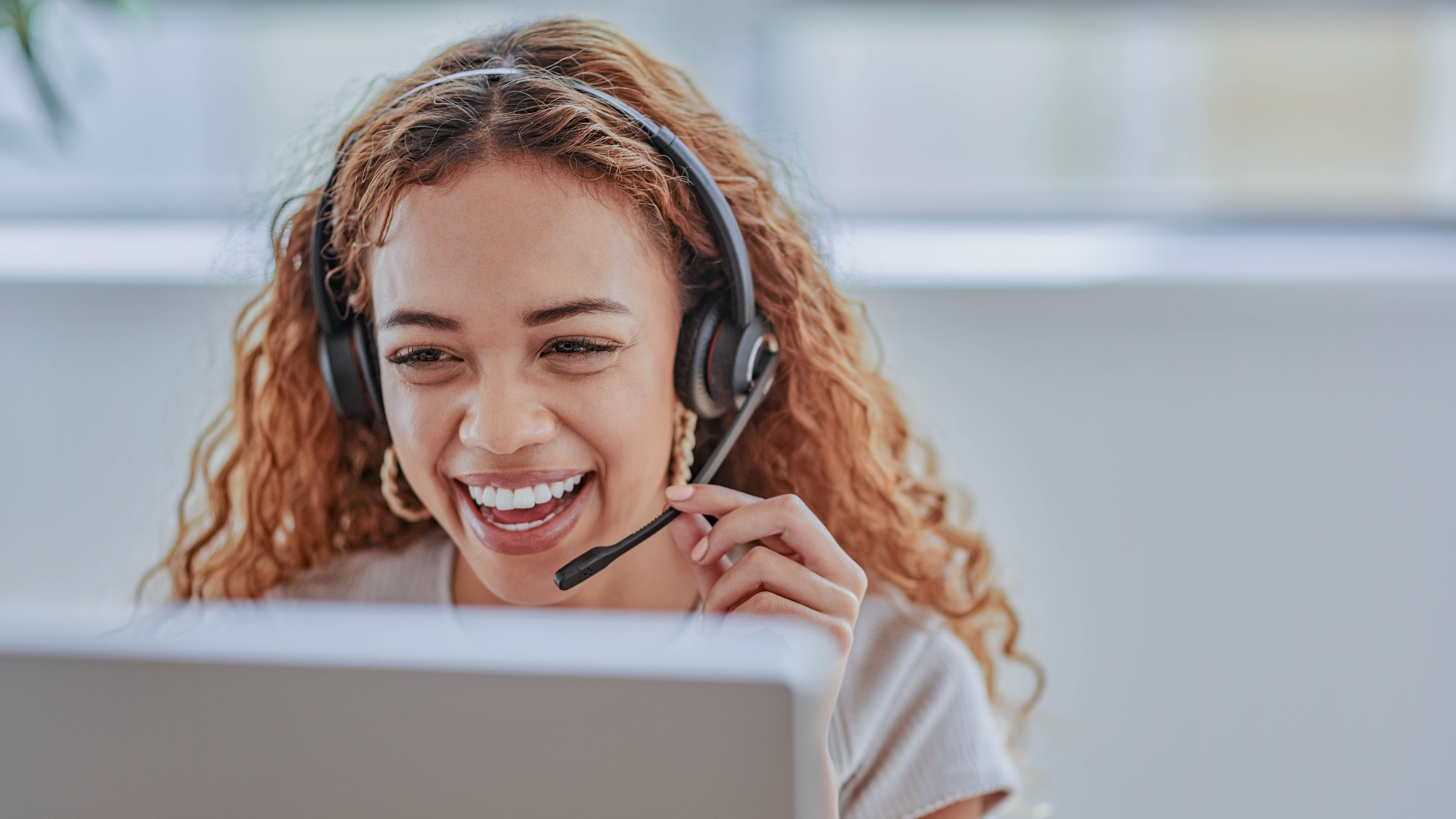 Lächelnde Frau mit Headset sitzt vor einem Laptop und spricht.