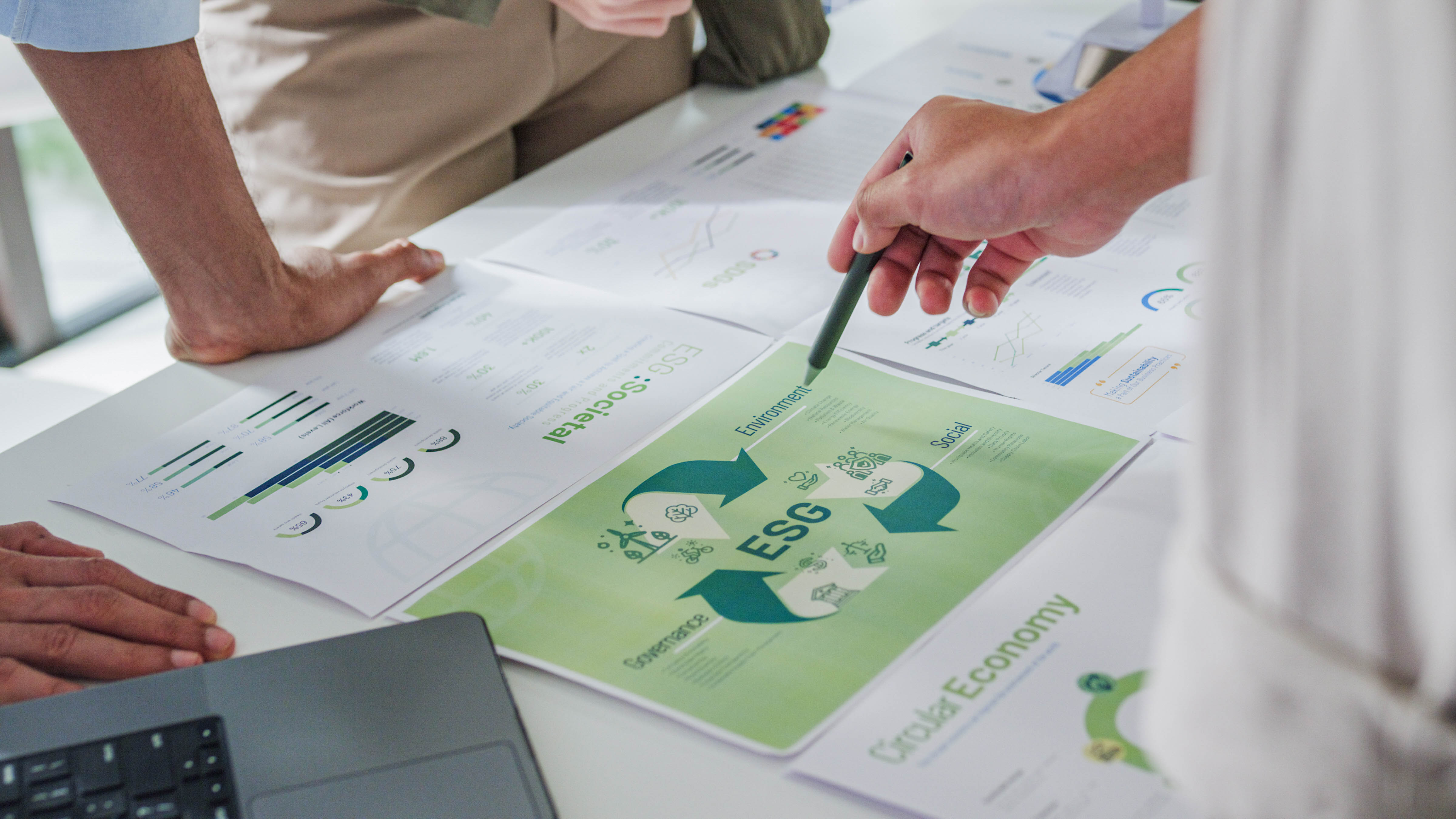 Hände zeigen auf Dokumente mit Grafiken und Informationen zu ESG (Umwelt, Soziales, Unternehmensführung) auf einem Tisch.