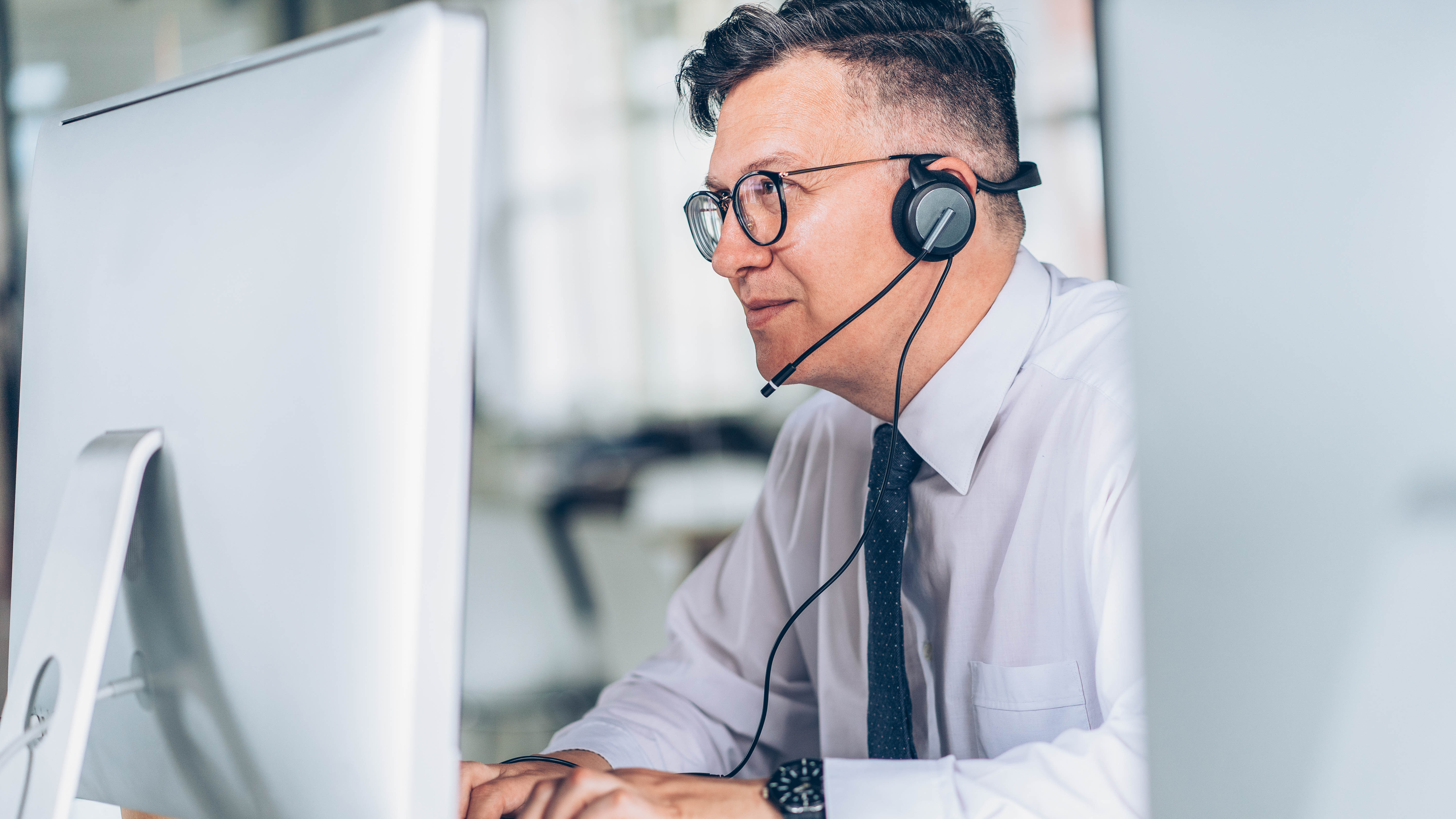 Mann mit Headset sitzt vor einem Computer und schaut konzentriert auf den Bildschirm.