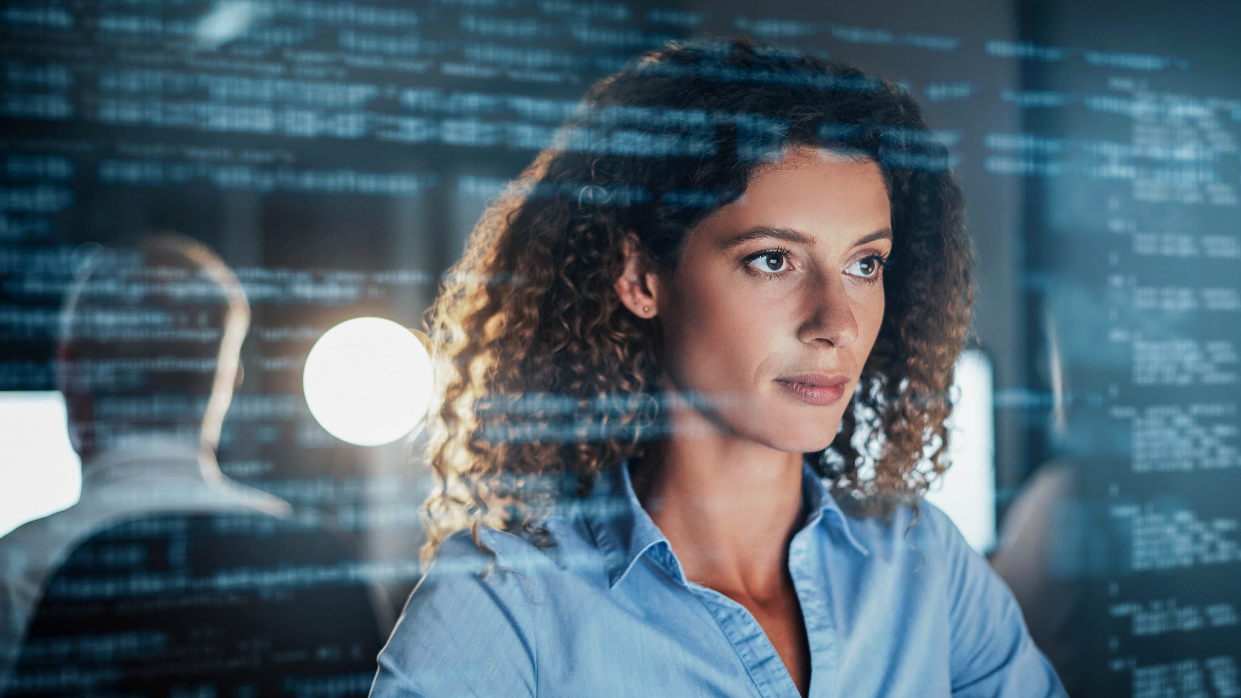 Frau mit lockigem Haar schaut konzentriert auf einen Bildschirm mit Code.