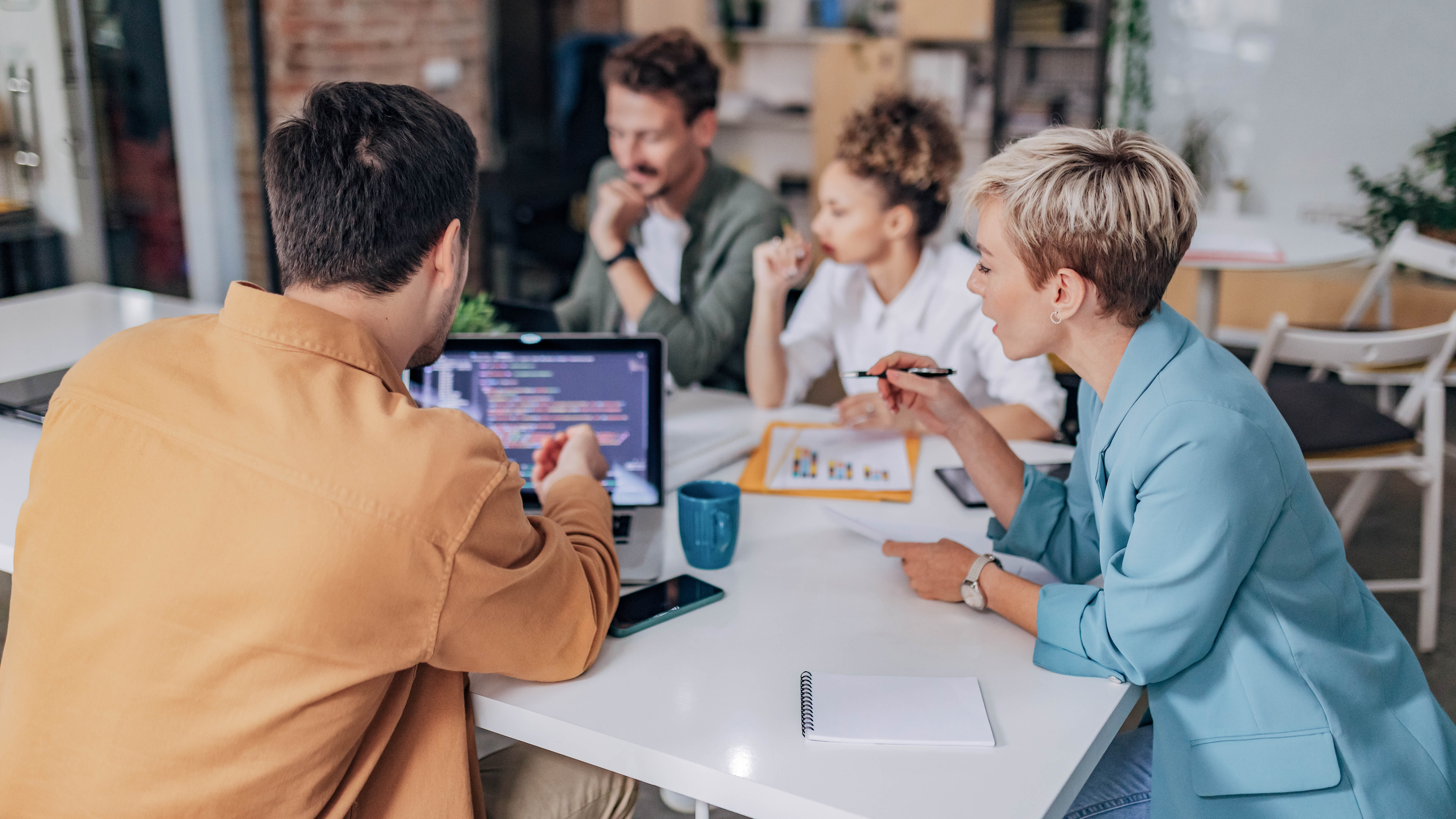 Fünf Personen sitzen an einem Tisch, diskutieren und schauen auf einen Laptop mit Programmiercode.