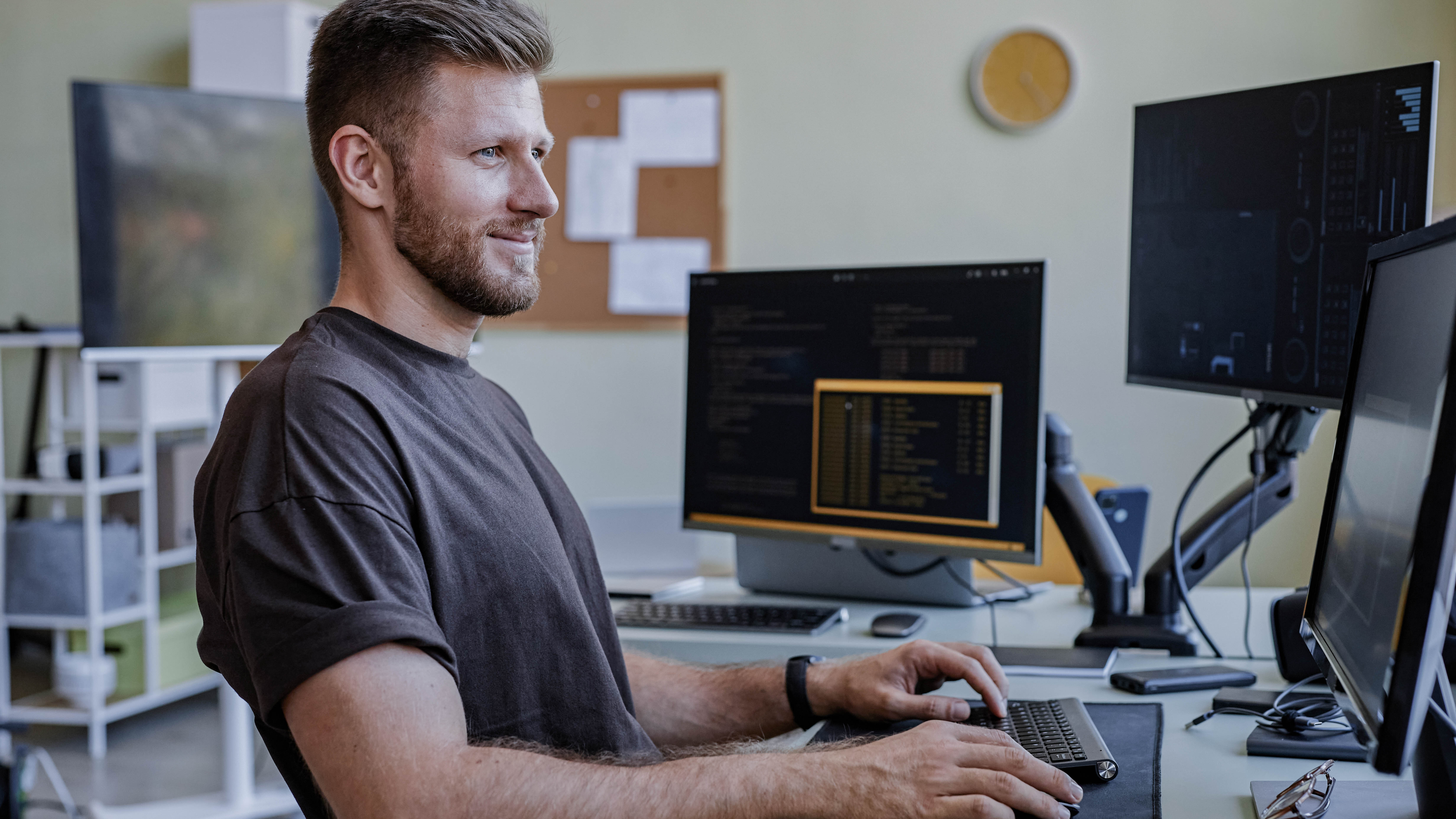 Mann sitzt an einem Schreibtisch mit mehreren Monitoren und arbeitet am Computer.