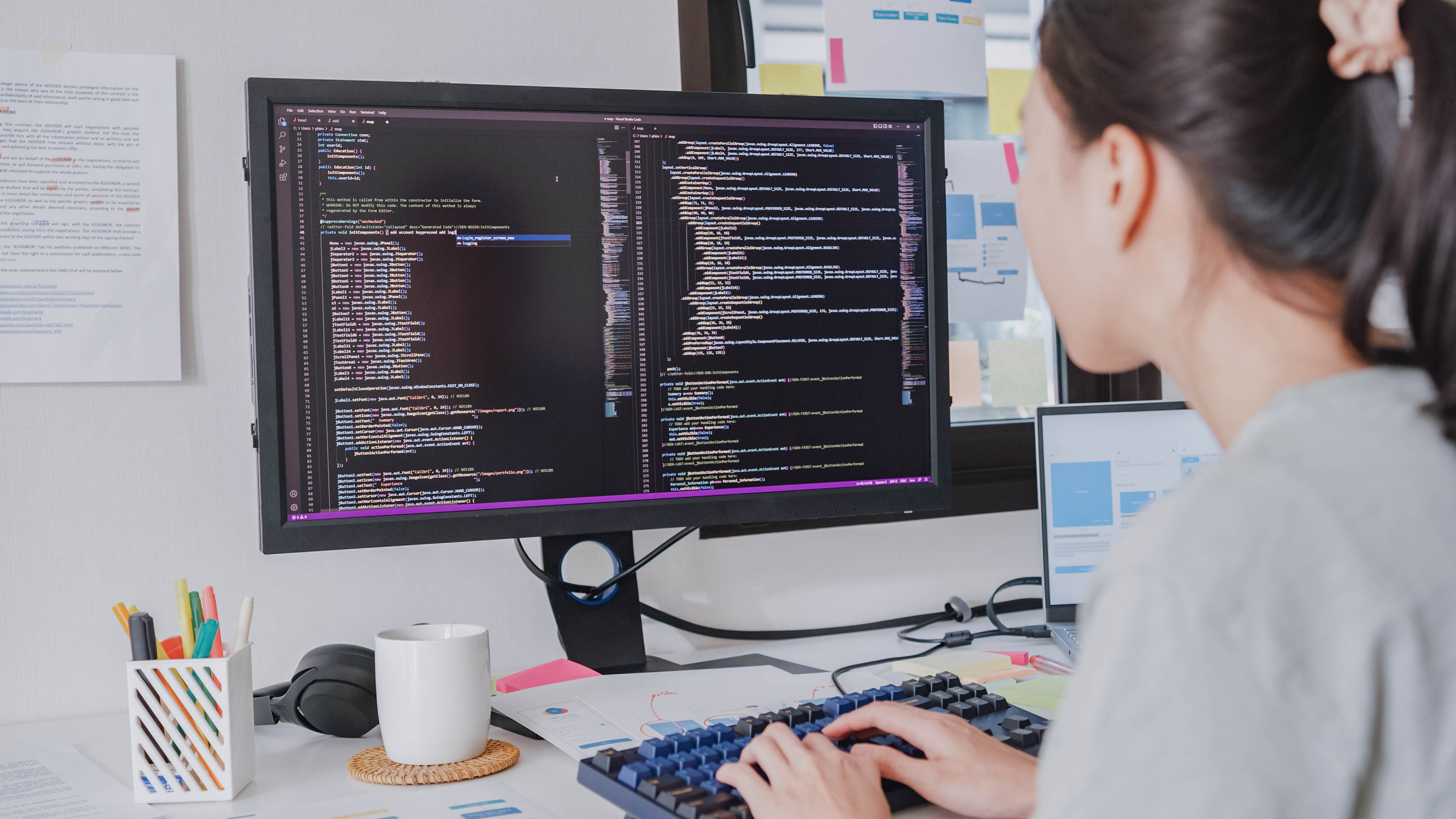 Eine Person sitzt am Schreibtisch und tippt auf einer Tastatur, während sie Code auf einem großen Monitor betrachtet.