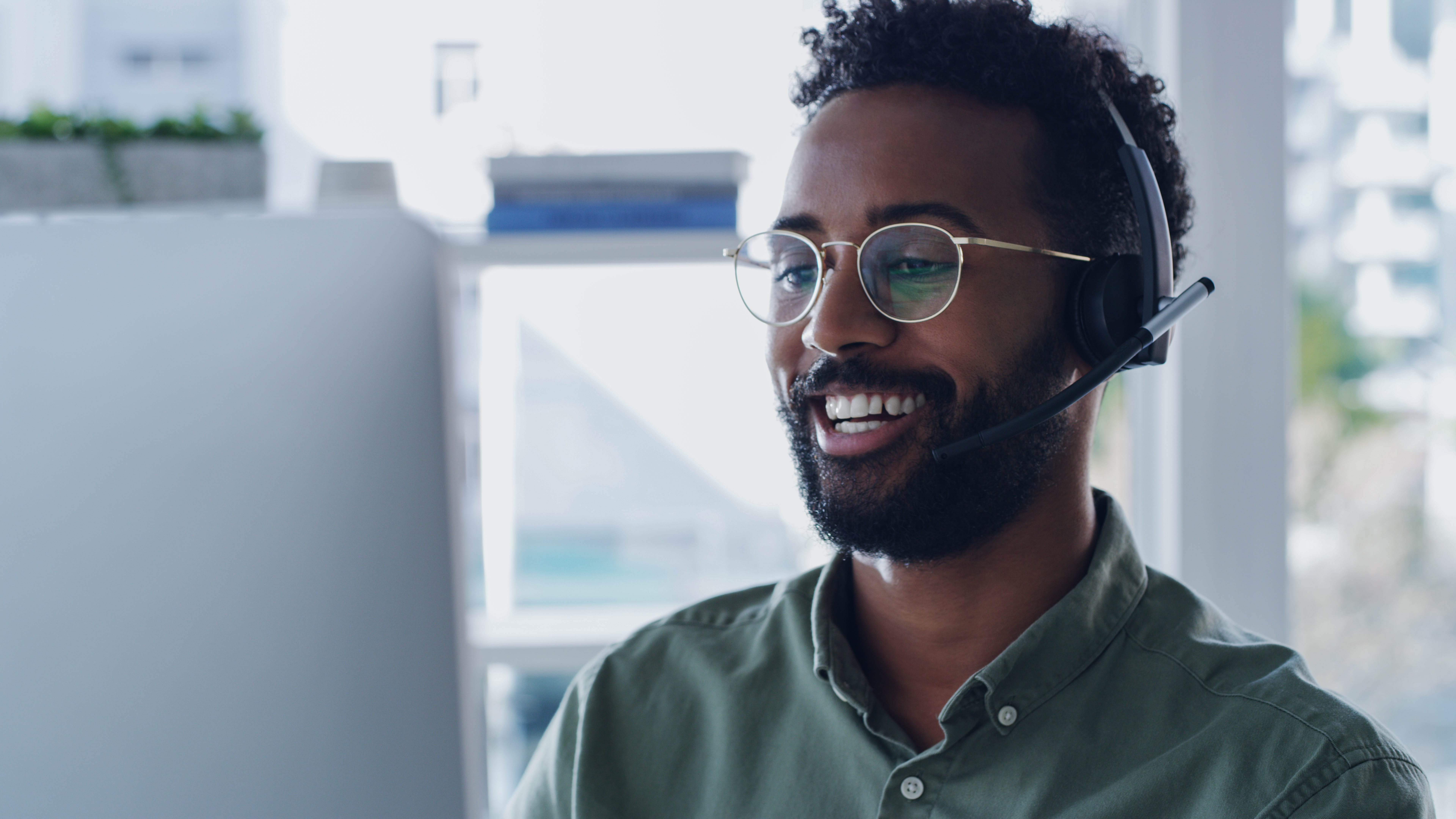 Mann mit Headset lächelt während eines Videoanrufs vor einem Computerbildschirm.