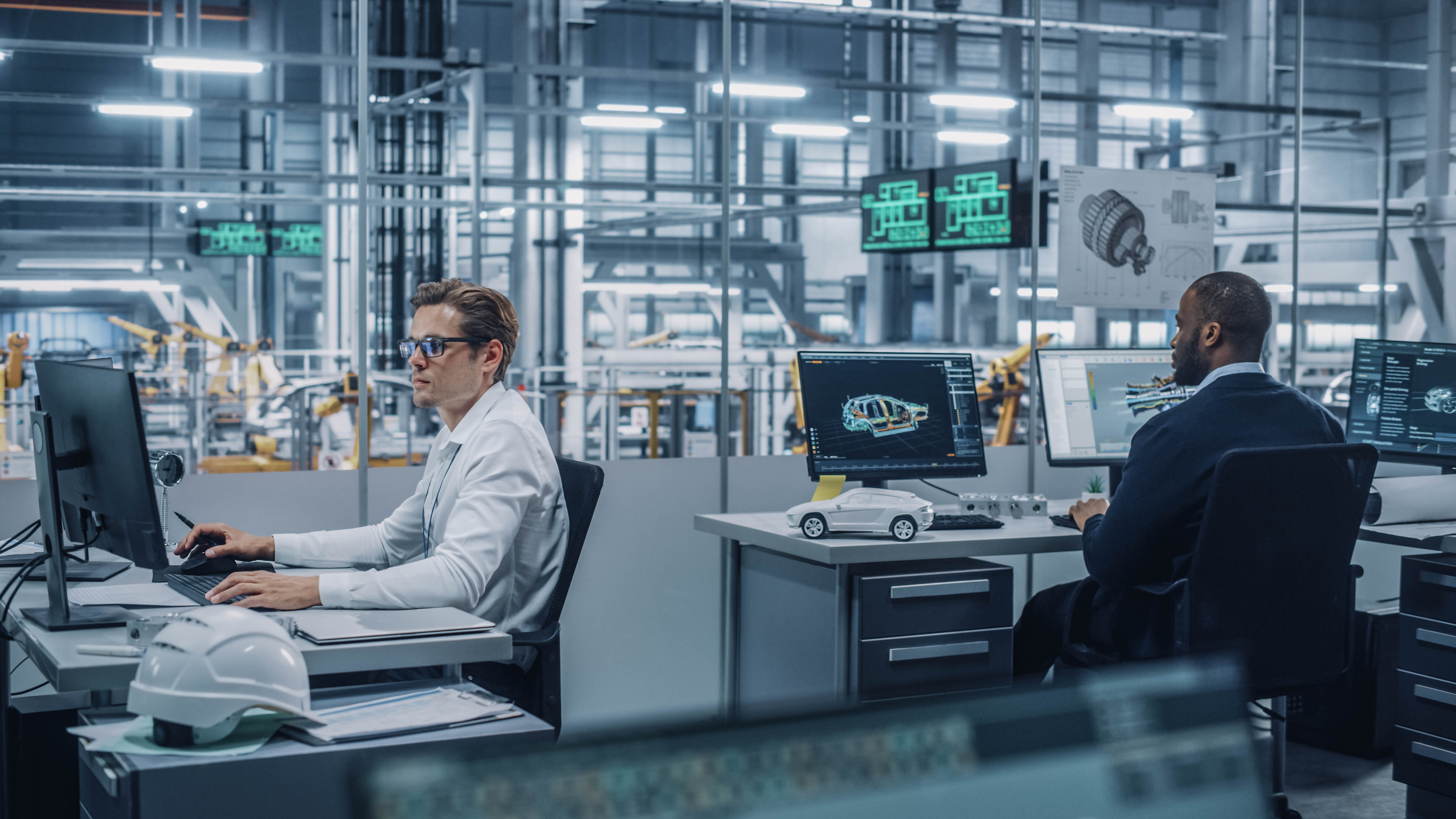 Zwei Ingenieure arbeiten an Computern in einem modernen Büro mit technischen Zeichnungen und einem Modell eines Autos.