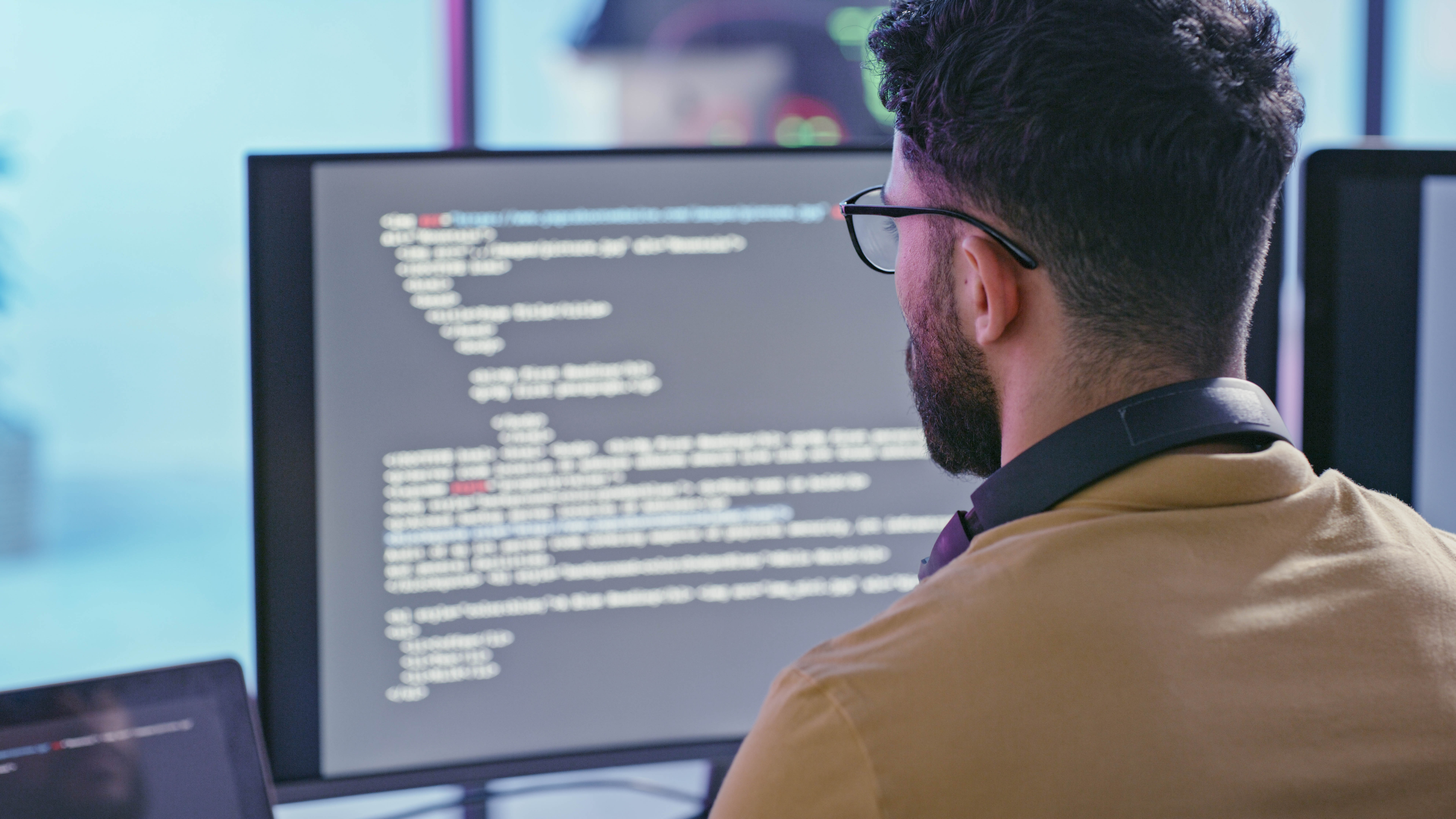 Mann mit Brille und Kopfhörern schaut auf einen Computerbildschirm mit Codezeilen.