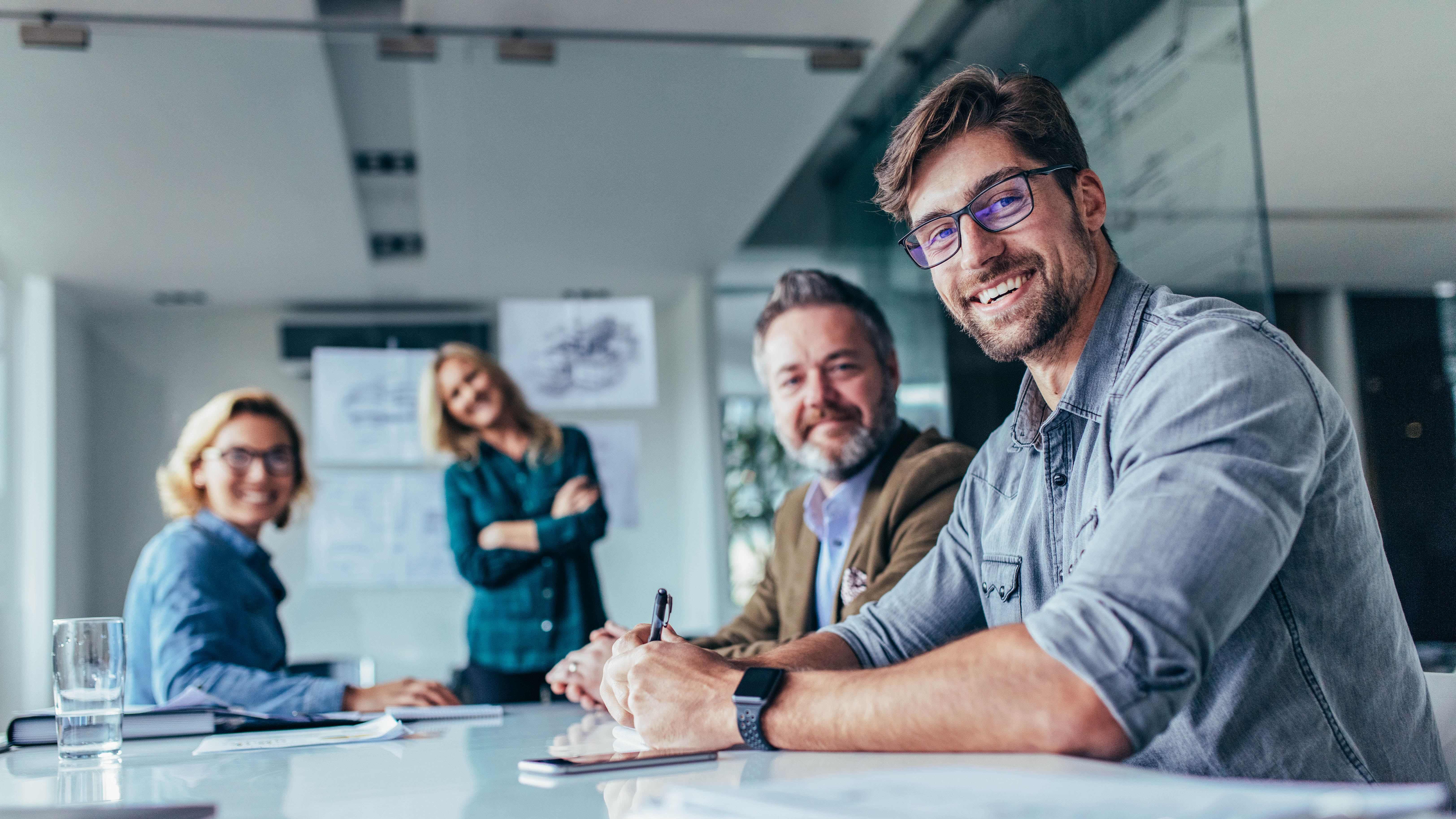 Vier Personen sitzen an einem Tisch in einem modernen Büro, lächeln und scheinen an einer Besprechung teilzunehmen.