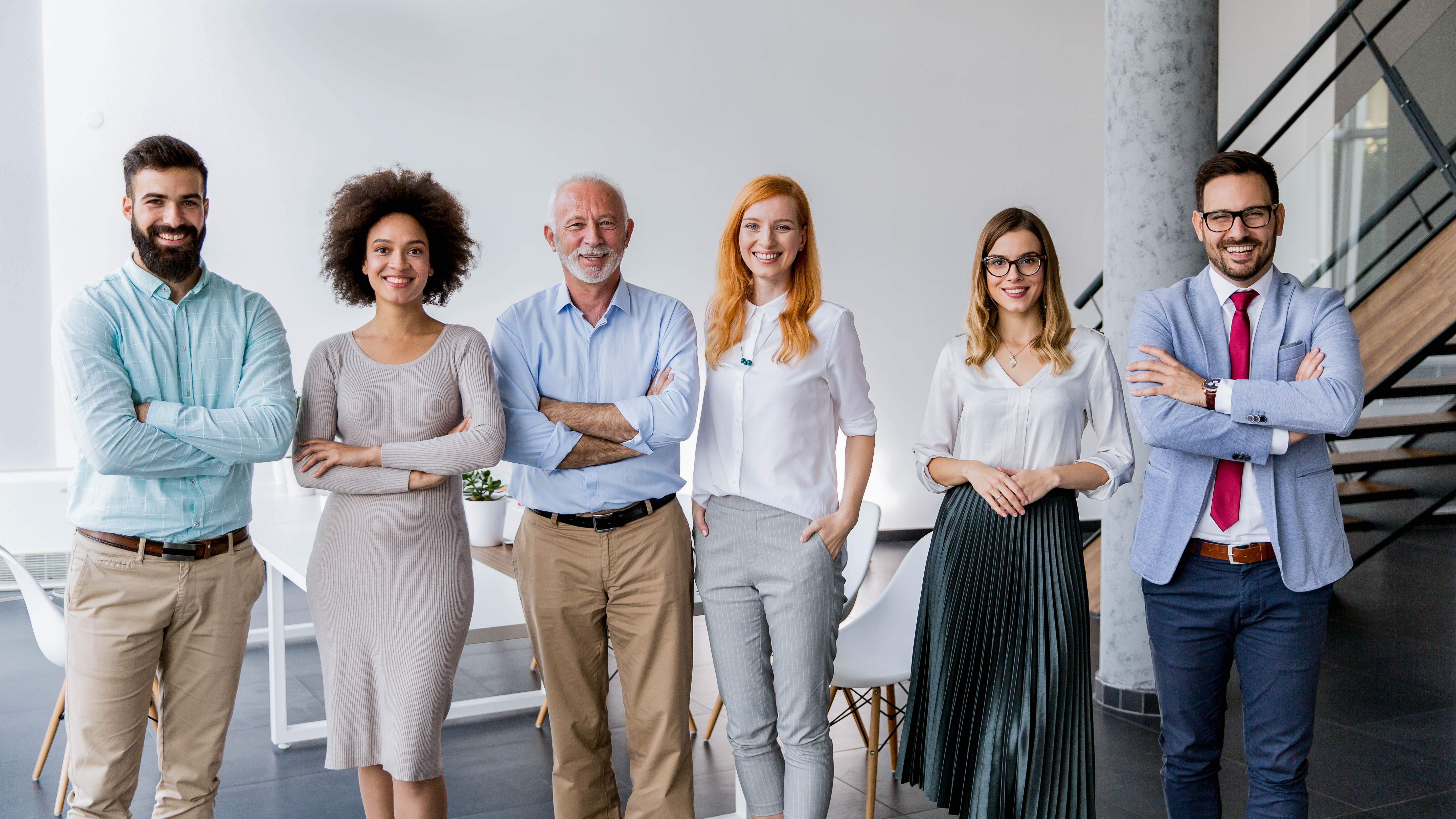 Sechs Personen stehen in einem modernen Büro, lächeln und haben die Arme verschränkt.
