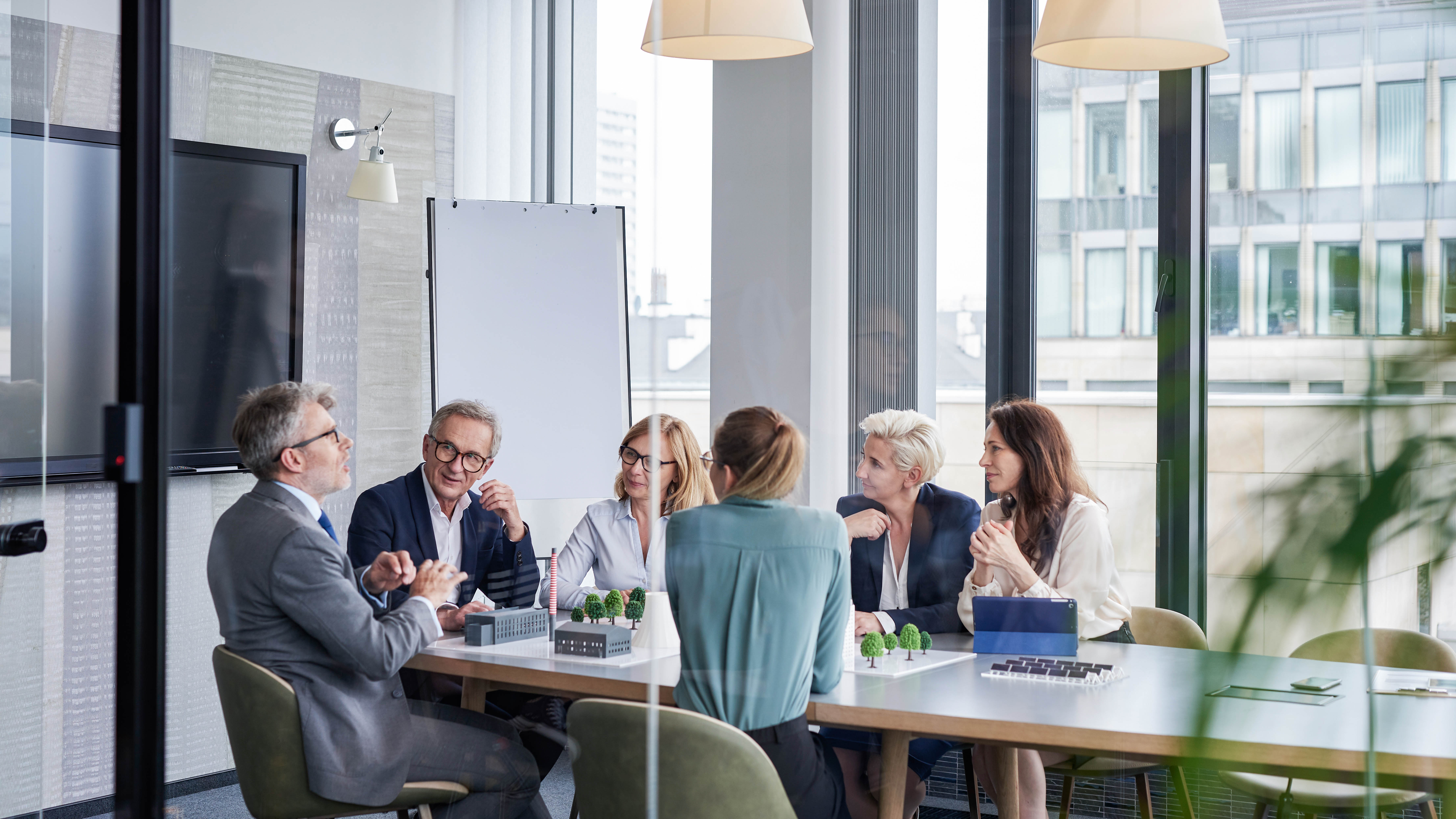 Eine Gruppe von sieben Personen in einem modernen Besprechungsraum diskutiert um einen Tisch mit Modellen und Notizen.
