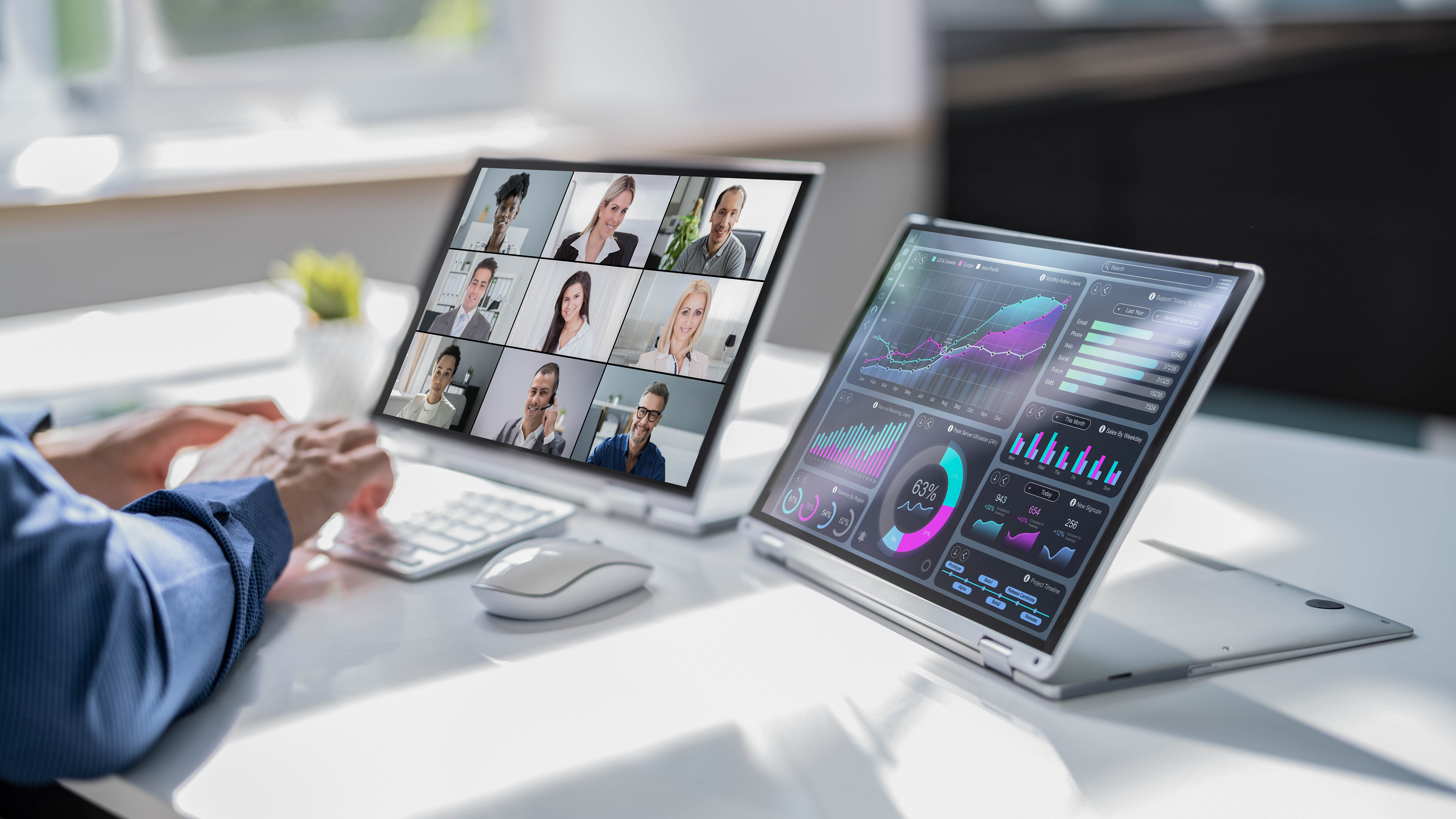 Hände tippen auf einer Tastatur, während zwei Laptops mit Videokonferenz und Datenanalysen angezeigt werden.