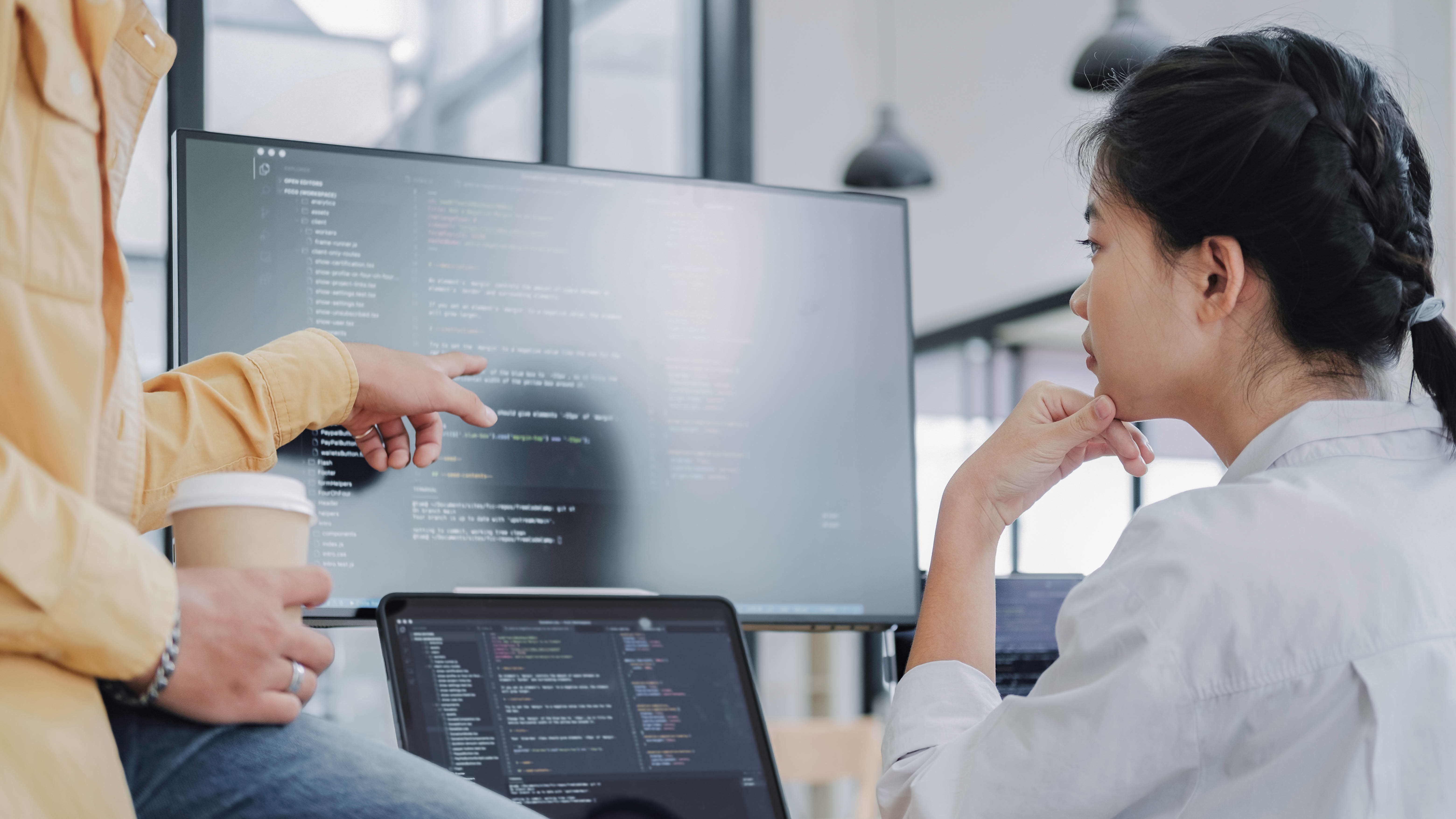 Zwei Personen diskutieren vor einem Computerbildschirm mit Code, eine Person zeigt auf den Bildschirm.